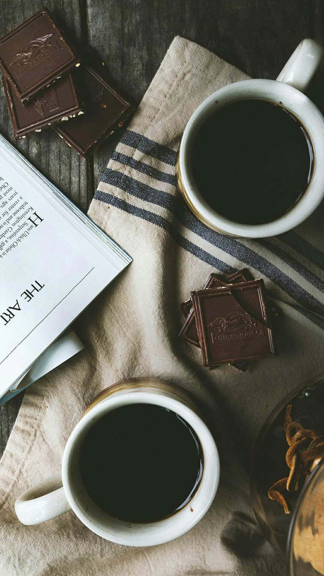 木桌上兩杯咖啡配朱古力條和一本書。