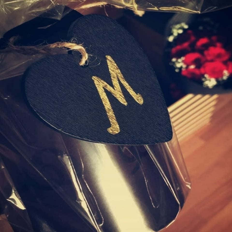 心形標籤，金色M，在塑膠包裝的禮物上，旁邊有紅玫瑰。