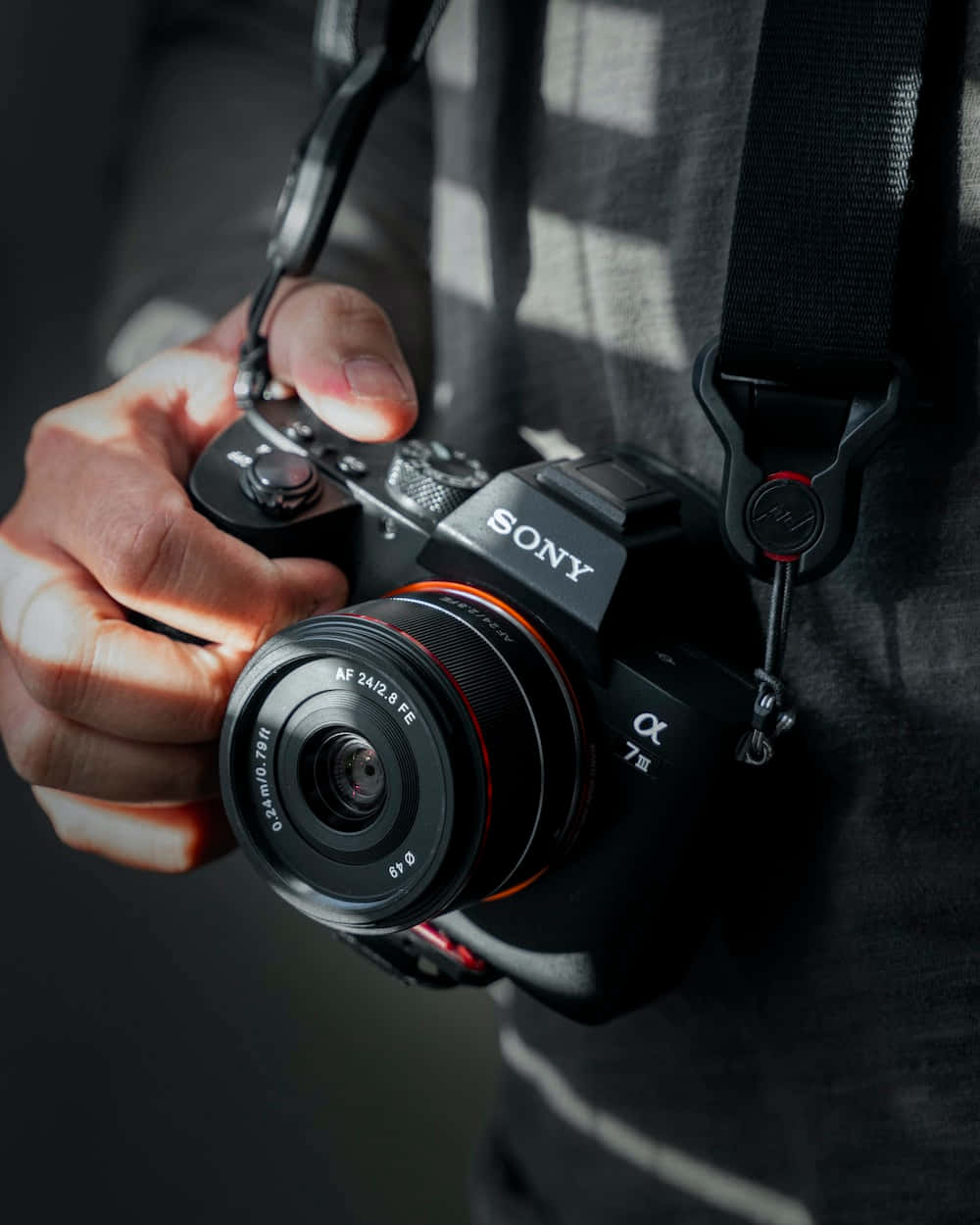 特寫一隻手拿著帶紅色鏡頭環的Sony Alpha 7 III相機。