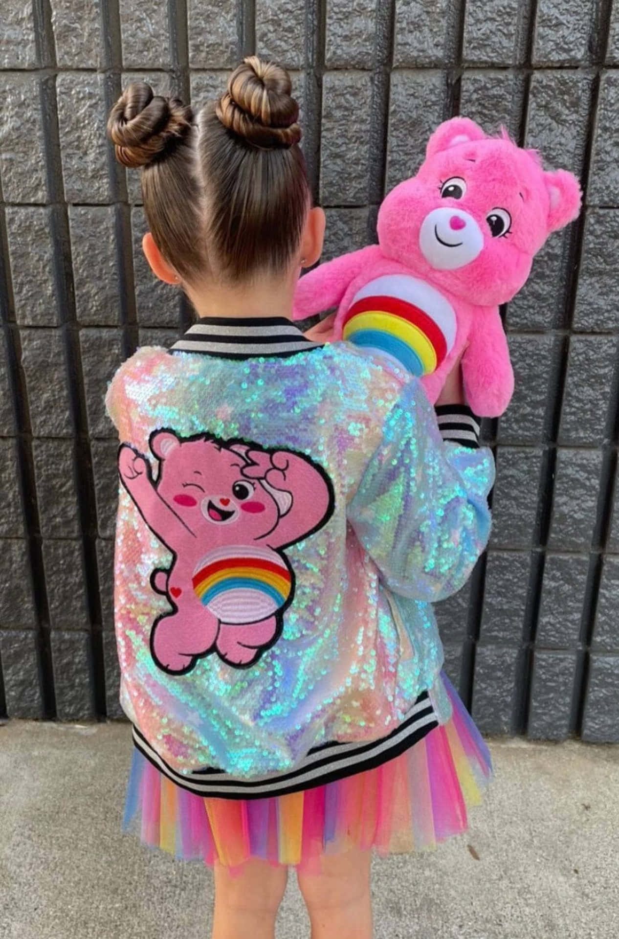 小孩穿著閃粉Care Bear外套和彩虹芭蕾舞裙，抱著毛絨熊。
