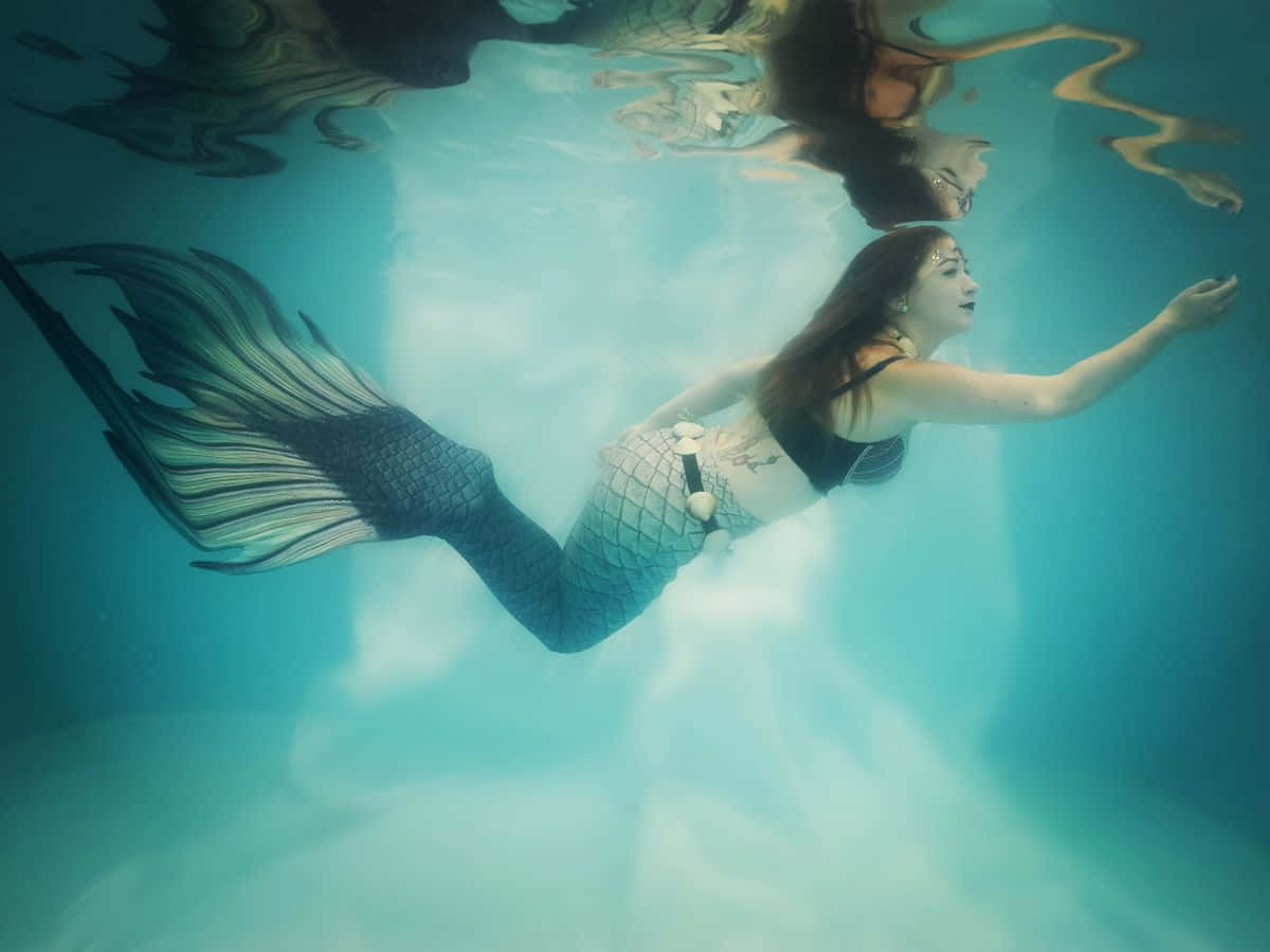 一位穿著美人魚尾巴的女性在陽光穿透水面的泳池中游泳。