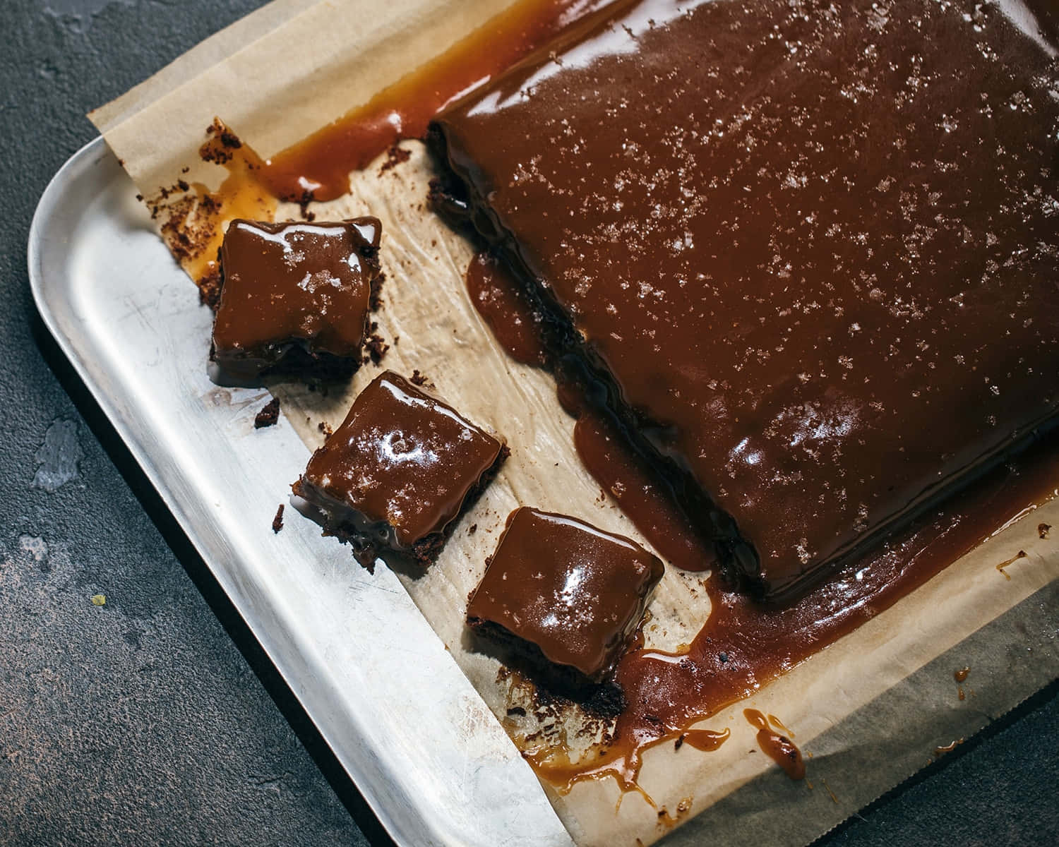 Caramel Brownie 桌布 壁紙 — 豐富的焦糖朱古力條，灑上薄片鹽，放在鋪有牛油紙的金屬托盤上。