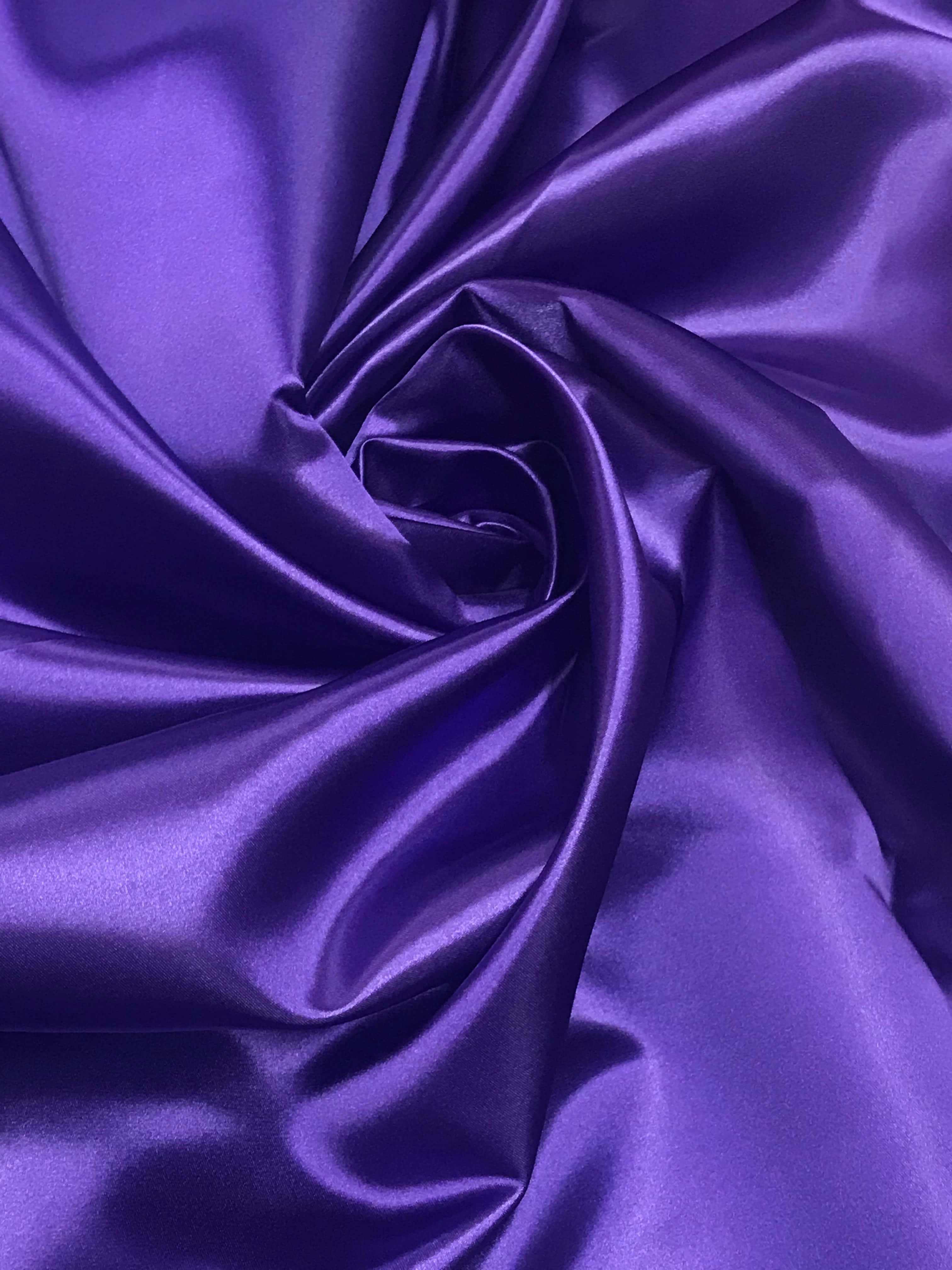 Purple Satin 桌布 壁紙 — 豐富的紫色緞布在柔軟的褶皺中旋轉，捕捉光線，呈現光澤亮面。