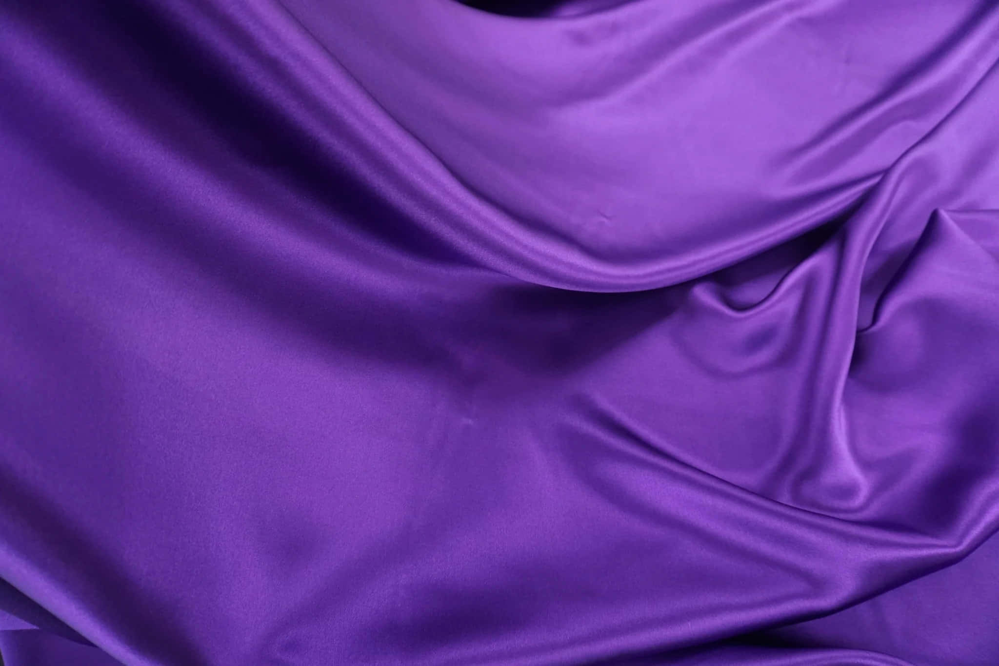 Purple Fabrics 桌布 壁紙 — 豐富的紫色緞面布料在柔軟的褶皺中流動，帶有光澤的高光和深沉的陰影，營造出奢華的質感。