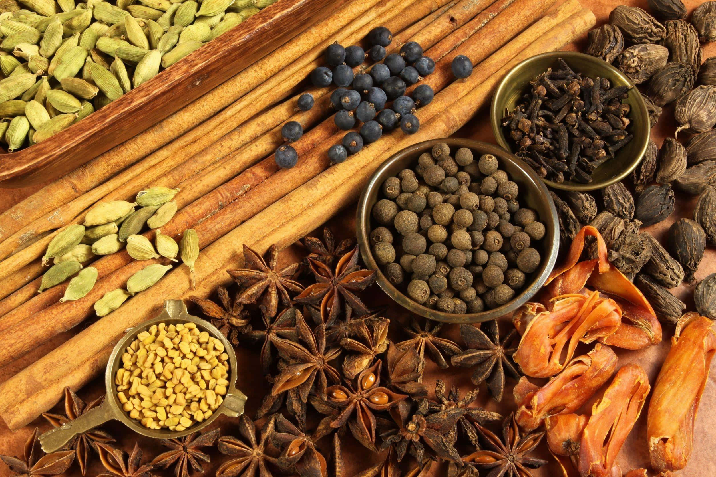 Spices 桌布 壁紙 — 豐富質感的完整香料，包括肉桂棒、小荳蔻、胡椒粒、八角茴香和丁香，排列在木質表面上。