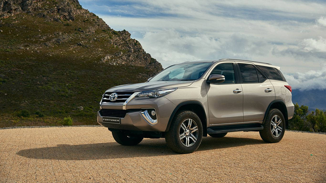 銀色豐田 Fortuner SUV 停泊在岩石地形和多雲天空的山路上。