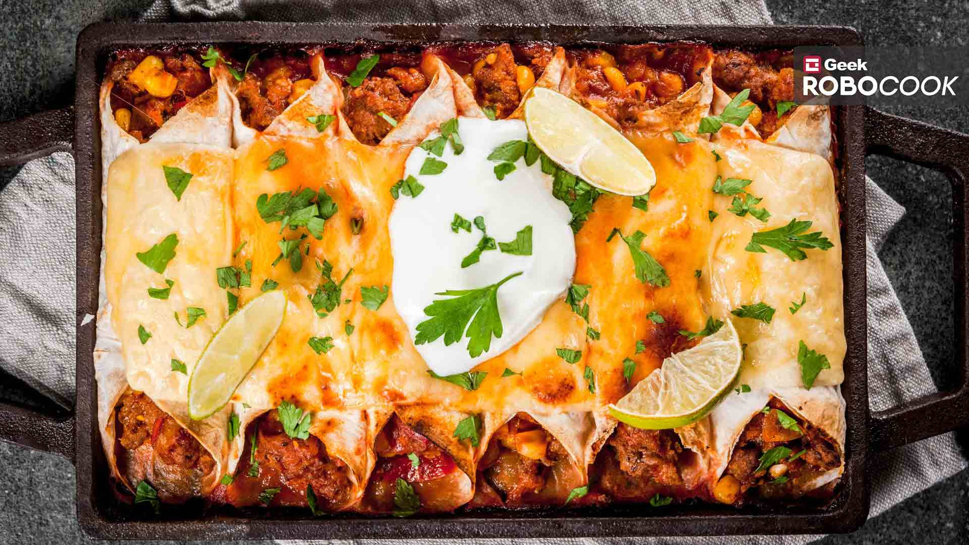 豐盛的墨西哥 enchiladas 盤，配以新鮮檸檬 壁紙 — 深色烤盤中的金黃色芝士辣醬玉米餅，上面放有酸奶油、青檸角和新鮮芫荽。