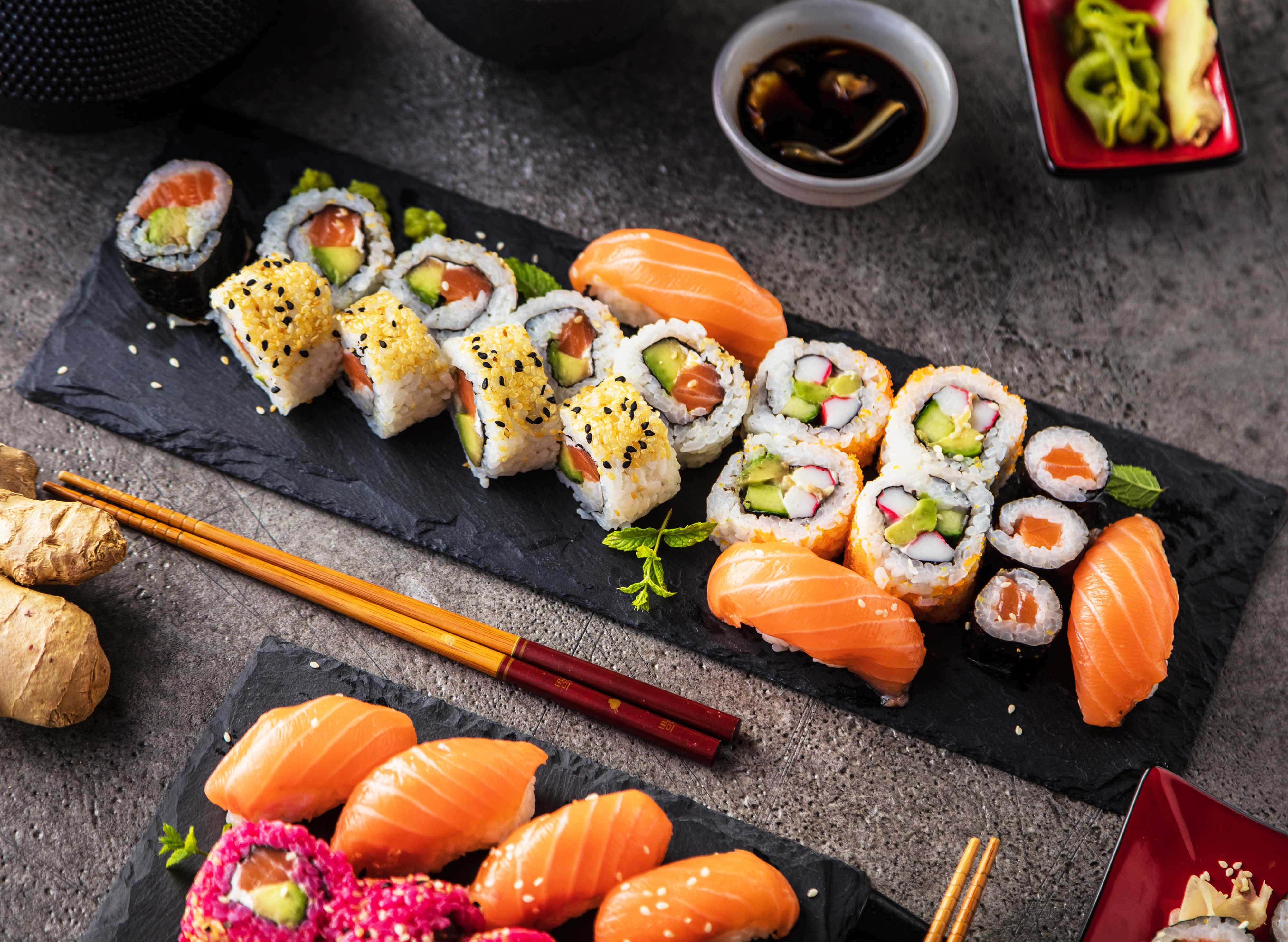 Sushi 桌布 壁紙 — 豐盛的壽司卷和刺身拼盤，藝術地擺放在石板盤上，配以醬油、生薑和芥末。