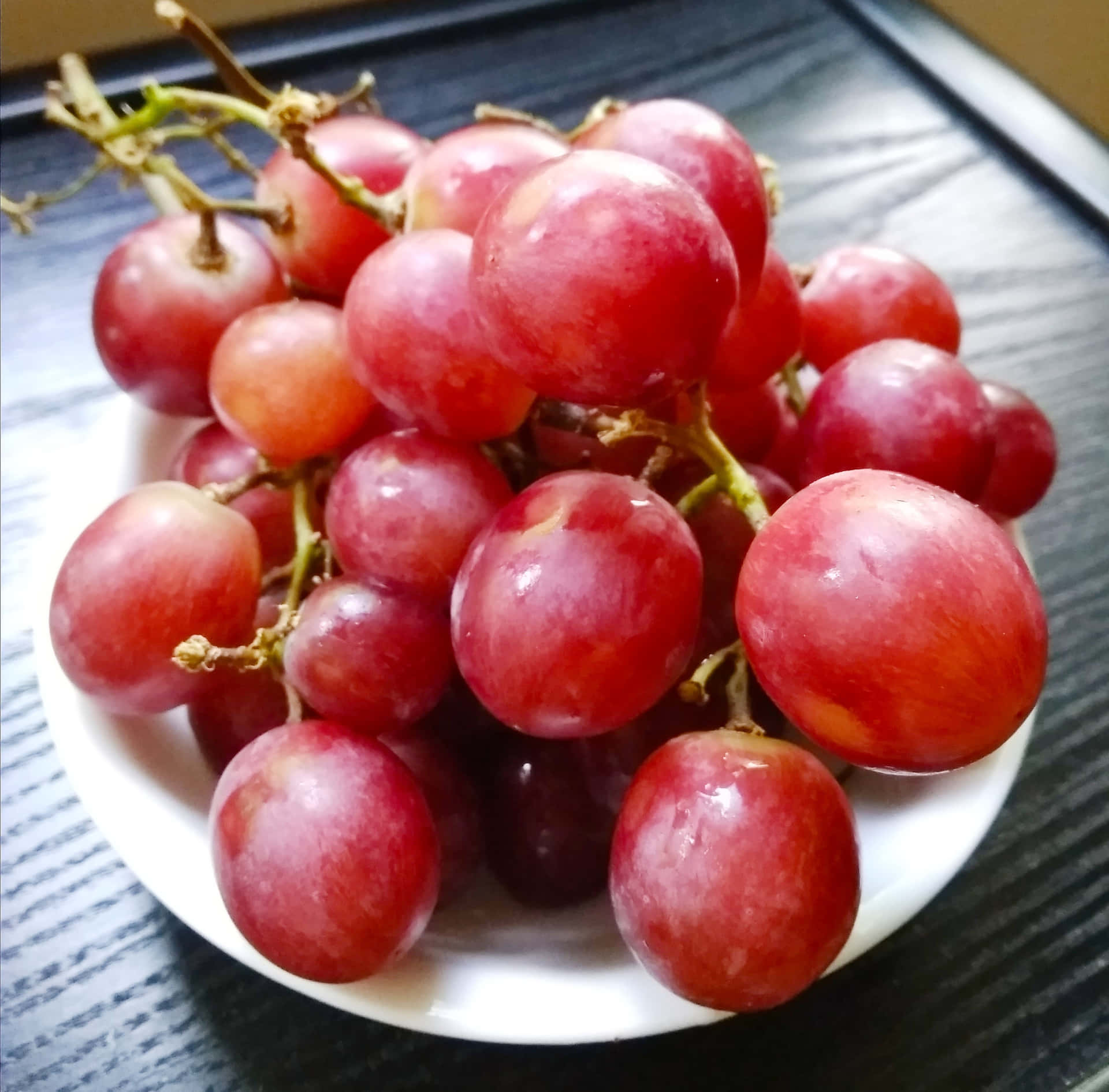 一碗飽滿的紅葡萄放在深色木質表面上。