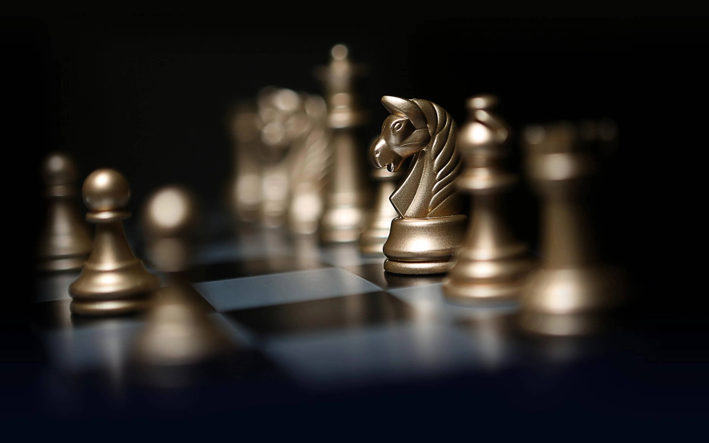 象棋強悍金騎士 壁紙 — 金色國際象棋棋子在淺景深的暗色棋盤上，於戲劇性燈光下閃耀。