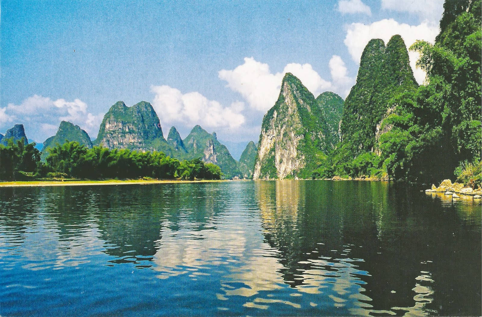 象牙海岸翠綠山脈全景 壁紙 — 高聳的喀斯特山脈覆蓋著茂密的綠色植物，在晴朗的天空和蓬鬆的雲朵下從平靜的藍色海水中升起。