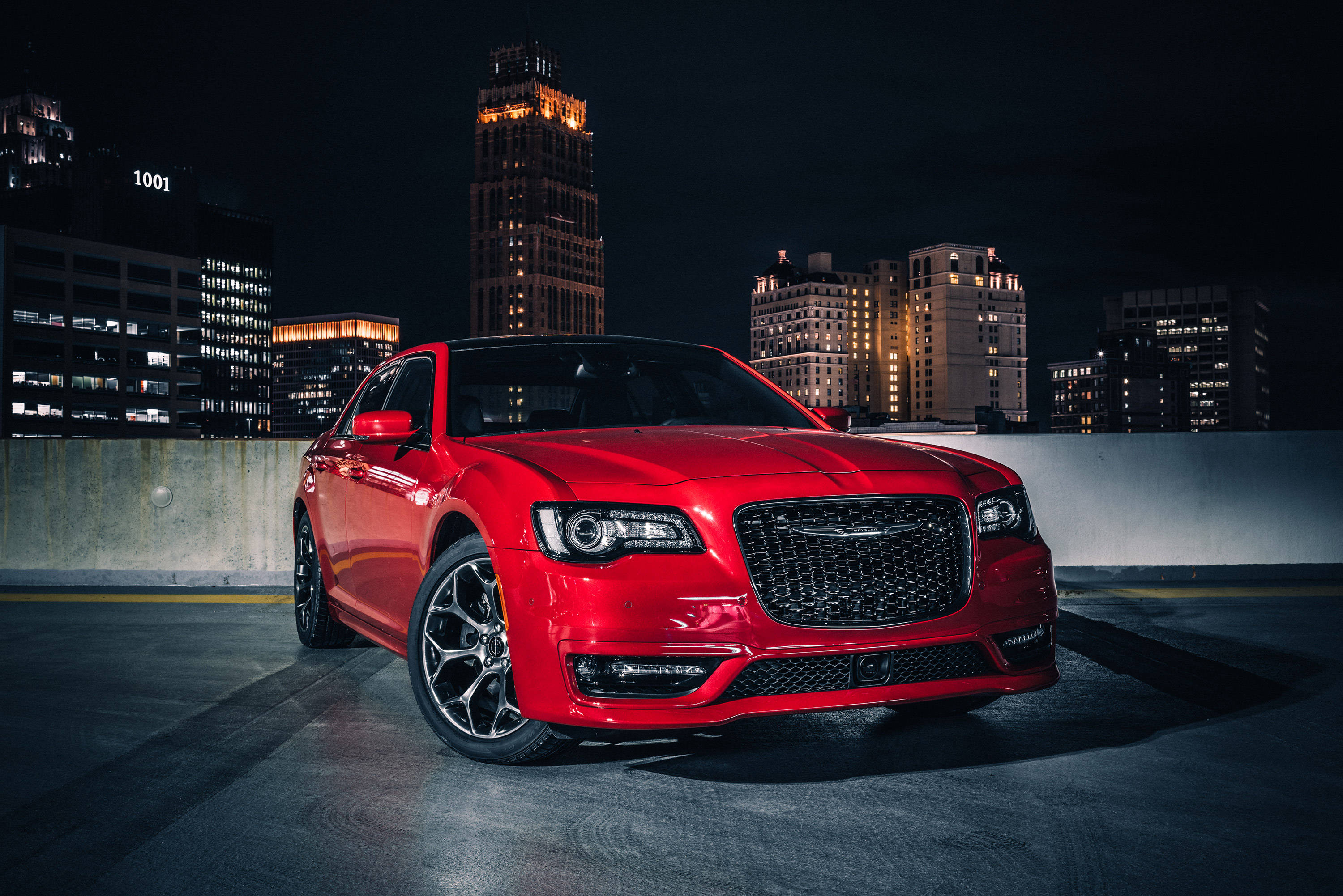 豪華 Chrysler 300 S 壁紙 — 一輛光亮的紅色豪華轎車在夜間停泊在天台上，背後是燈火通明的摩天大樓，在都市燈光下閃爍。