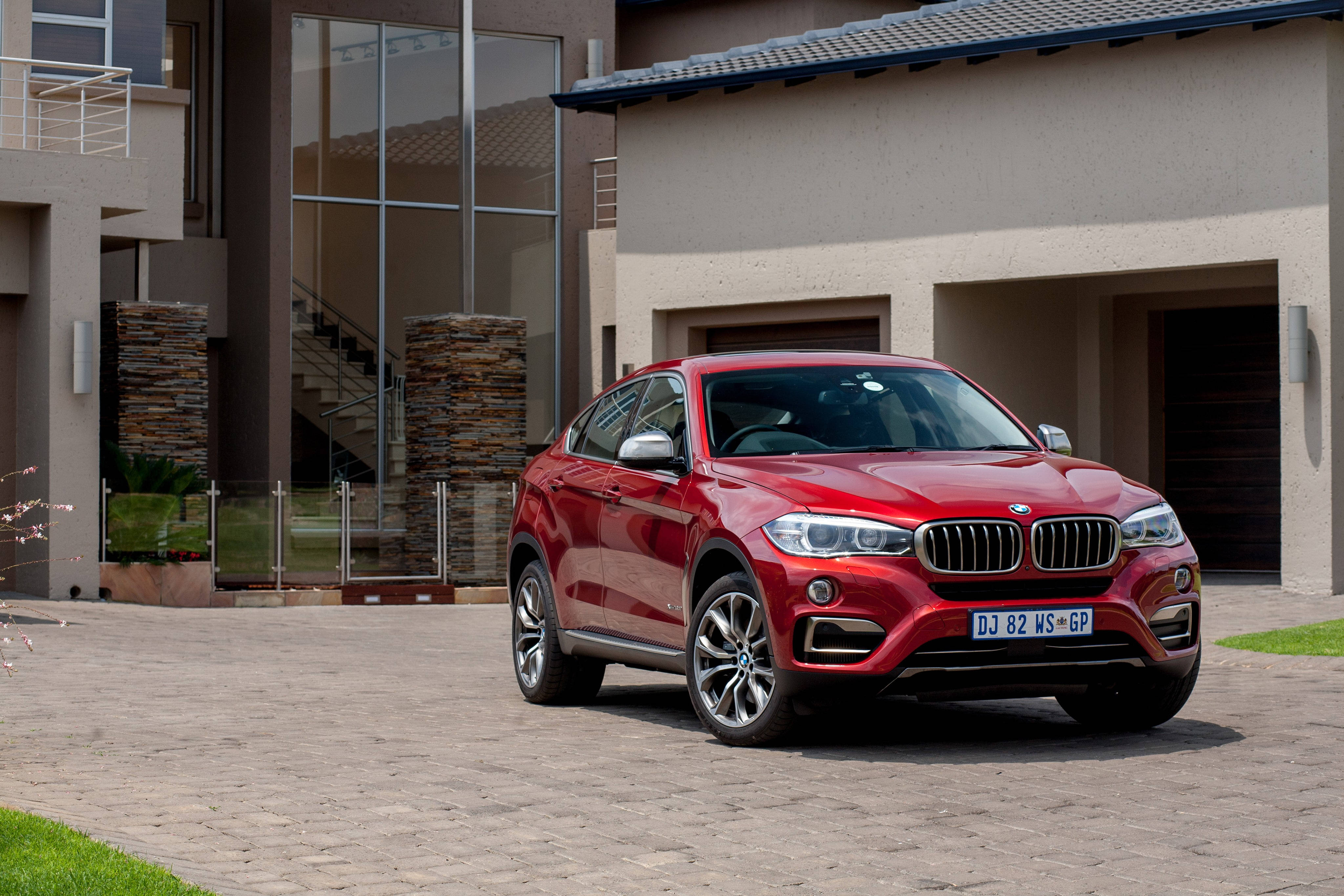 豪華BMW X6 M停於現代住宅外 壁紙 — 一架亮紅色BMW X6 SUV停泊在現代化房屋前的石頭車道上，房屋有玻璃牆和石柱。