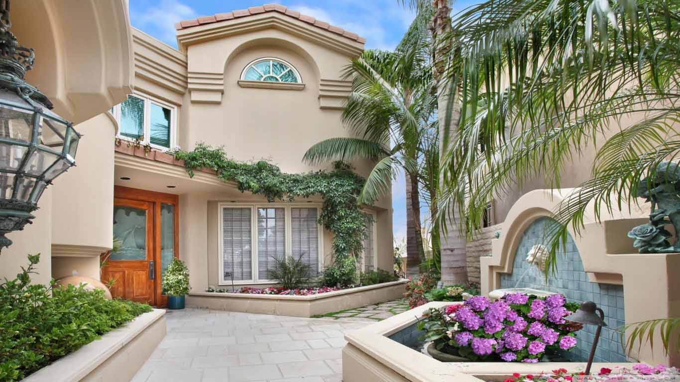 豪華的米色地中海風格住宅，庭院中有棕櫚樹和紫色花朵。