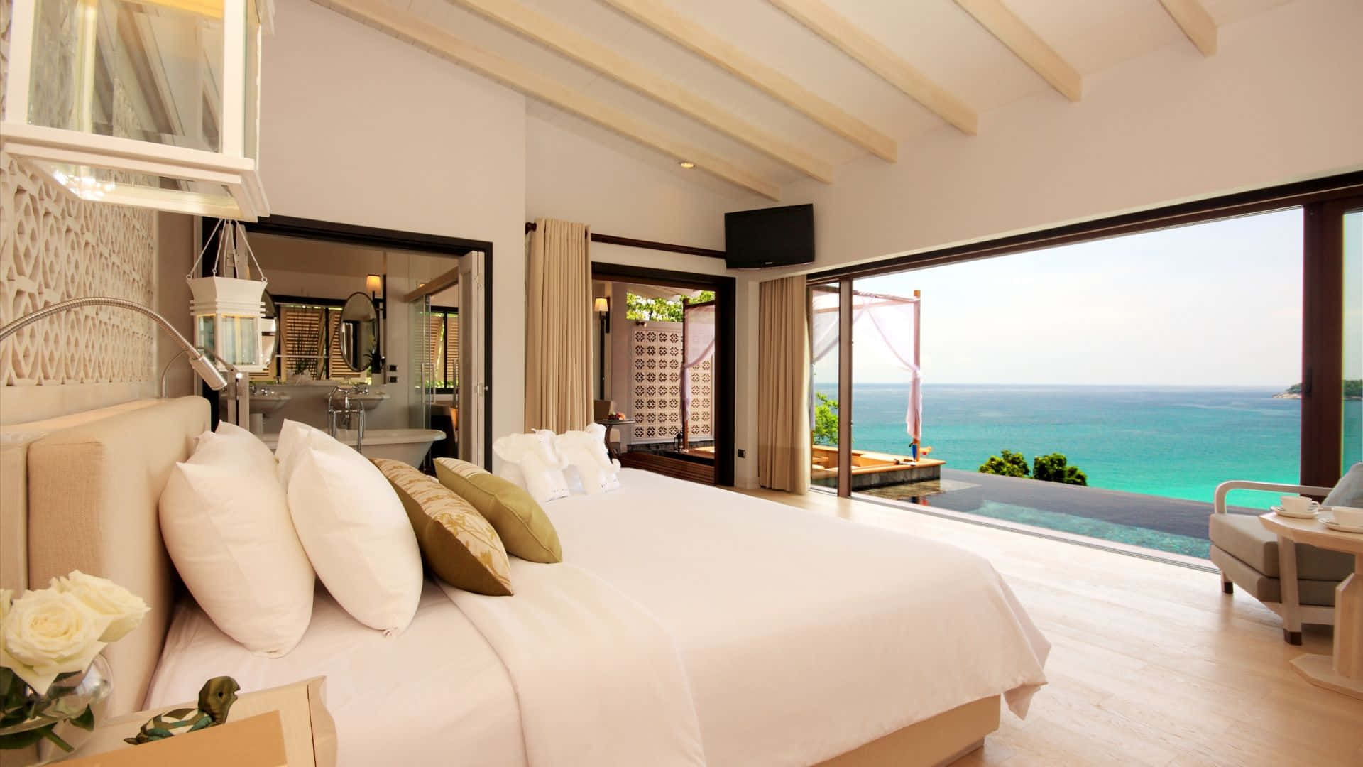 Hotel Room 桌布 壁紙 — 豪華海景臥室，配有一張大床、白色床單和木樑，俯瞰碧綠色的海洋。