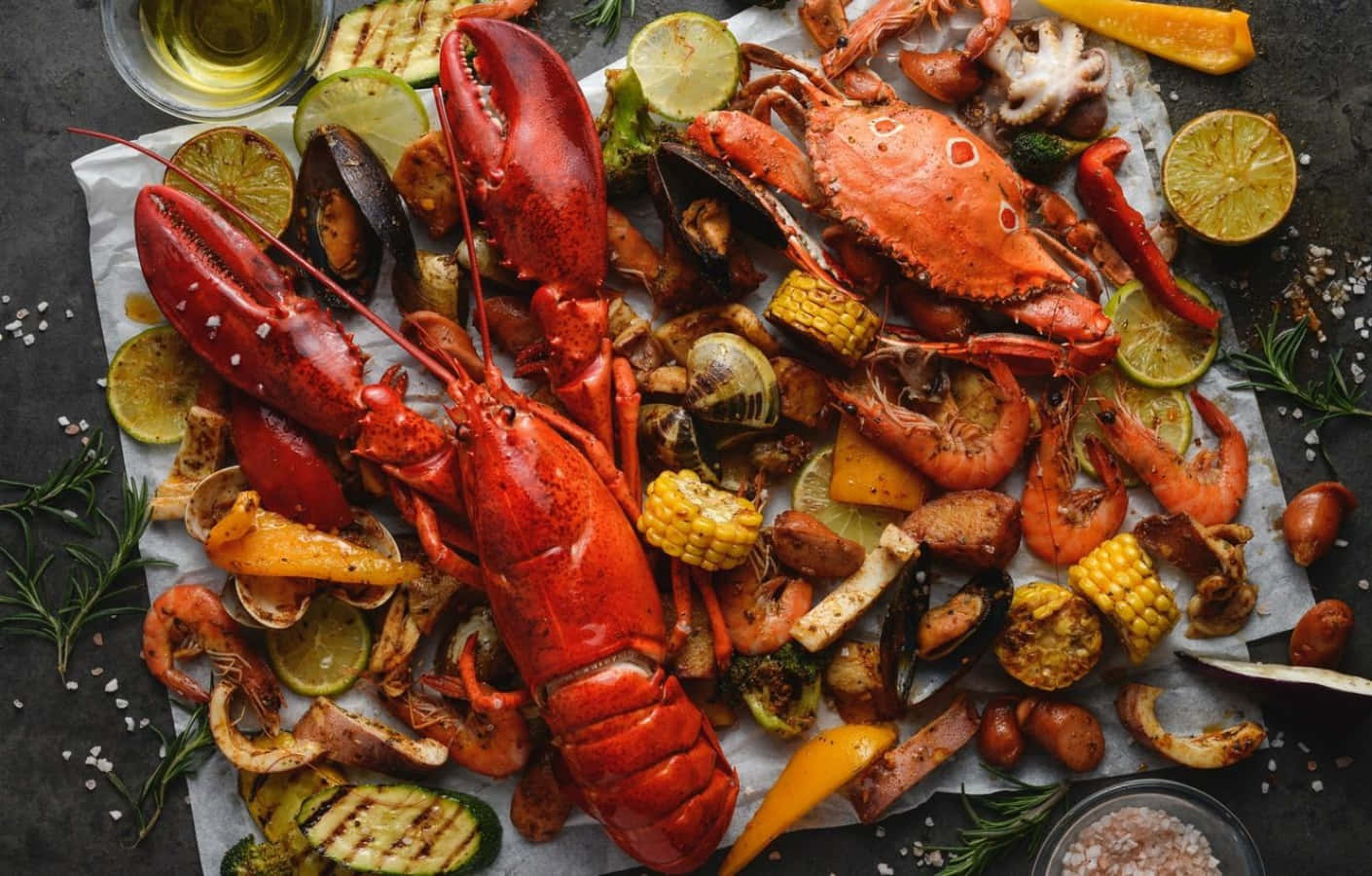 Seafood 桌布 壁紙 — 豪華海鮮蒸煮大餐，包括巨型紅龍蝦、蟹、蝦、粟米和蔬菜，放在牛油紙上，配以青檸片和香草。