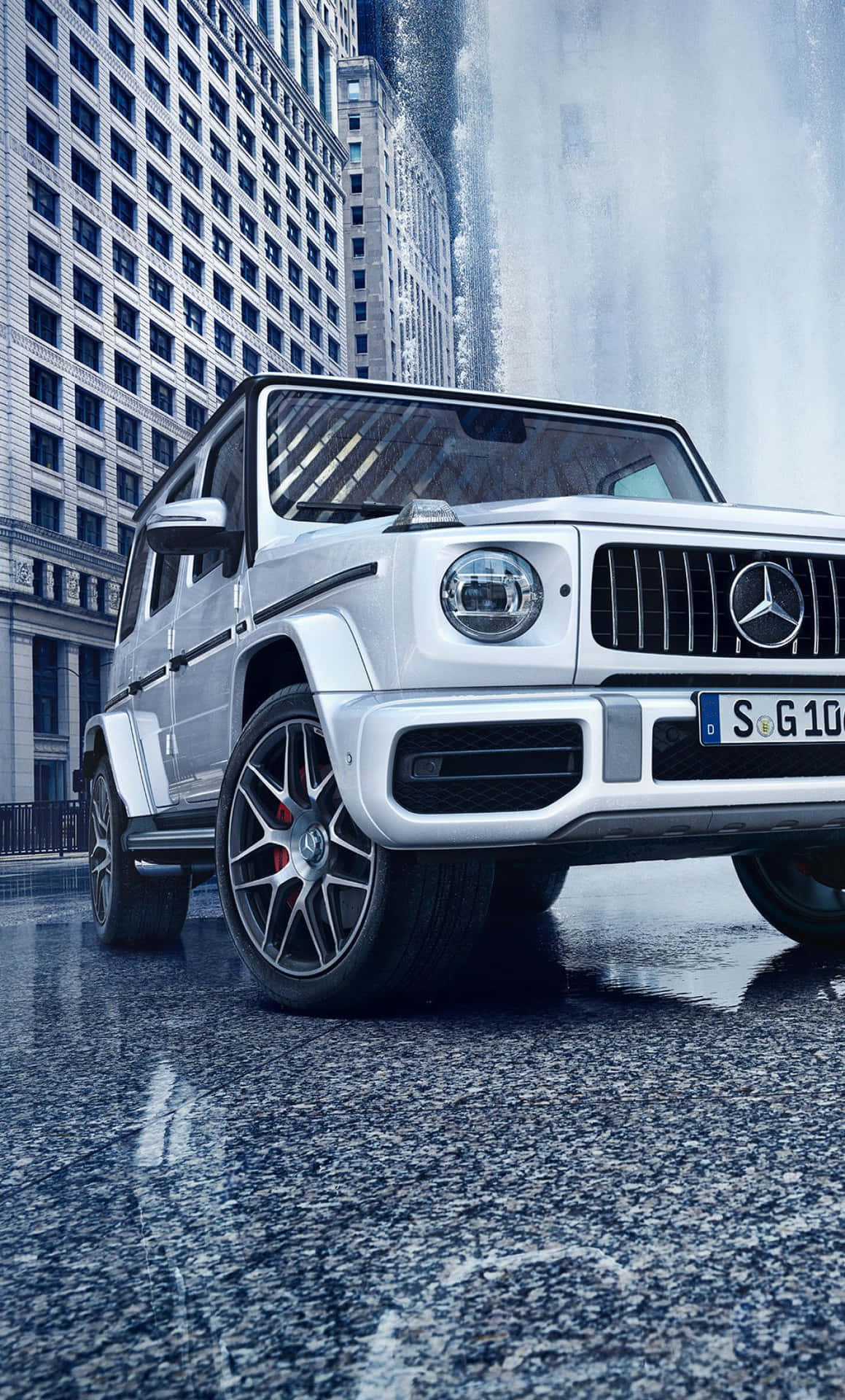 銀色 Mercedes G-Class SUV 停在瀑布和摩天大樓附近的濕漉漉街道上。