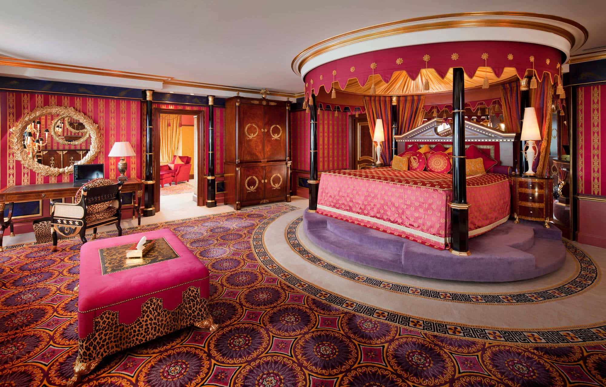 Hotel 桌布 壁紙 — 豪華睡房，配備圓形天蓬床，以洋紅色布料和金色飾邊裝飾，周圍是華麗圖案地毯和濃郁的紅色牆壁。