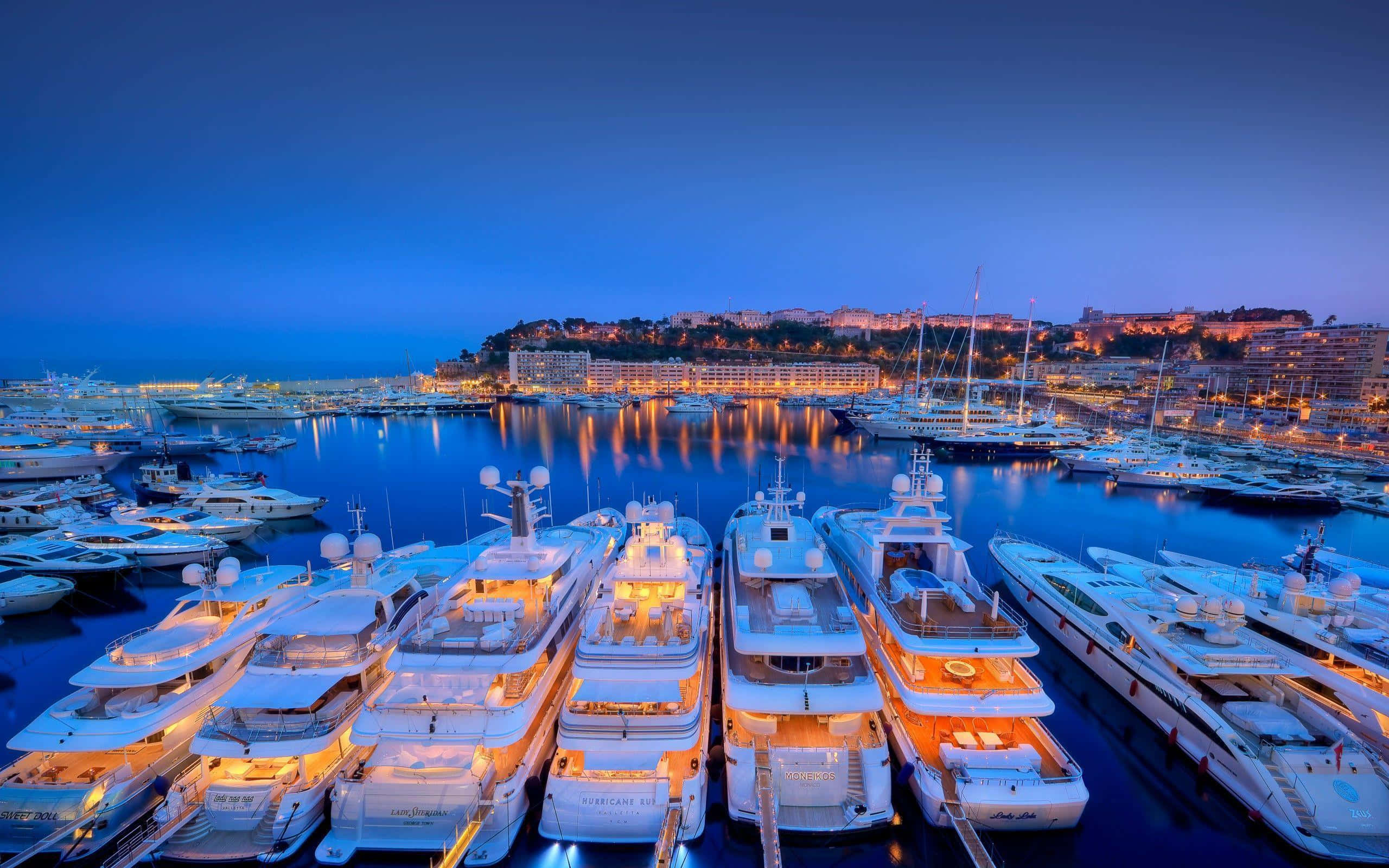 Yacht 桌布 壁紙 — 豪華遊艇在黃昏時分的繁忙港口中溫暖地發光，城市燈光倒映在平靜的水面上。