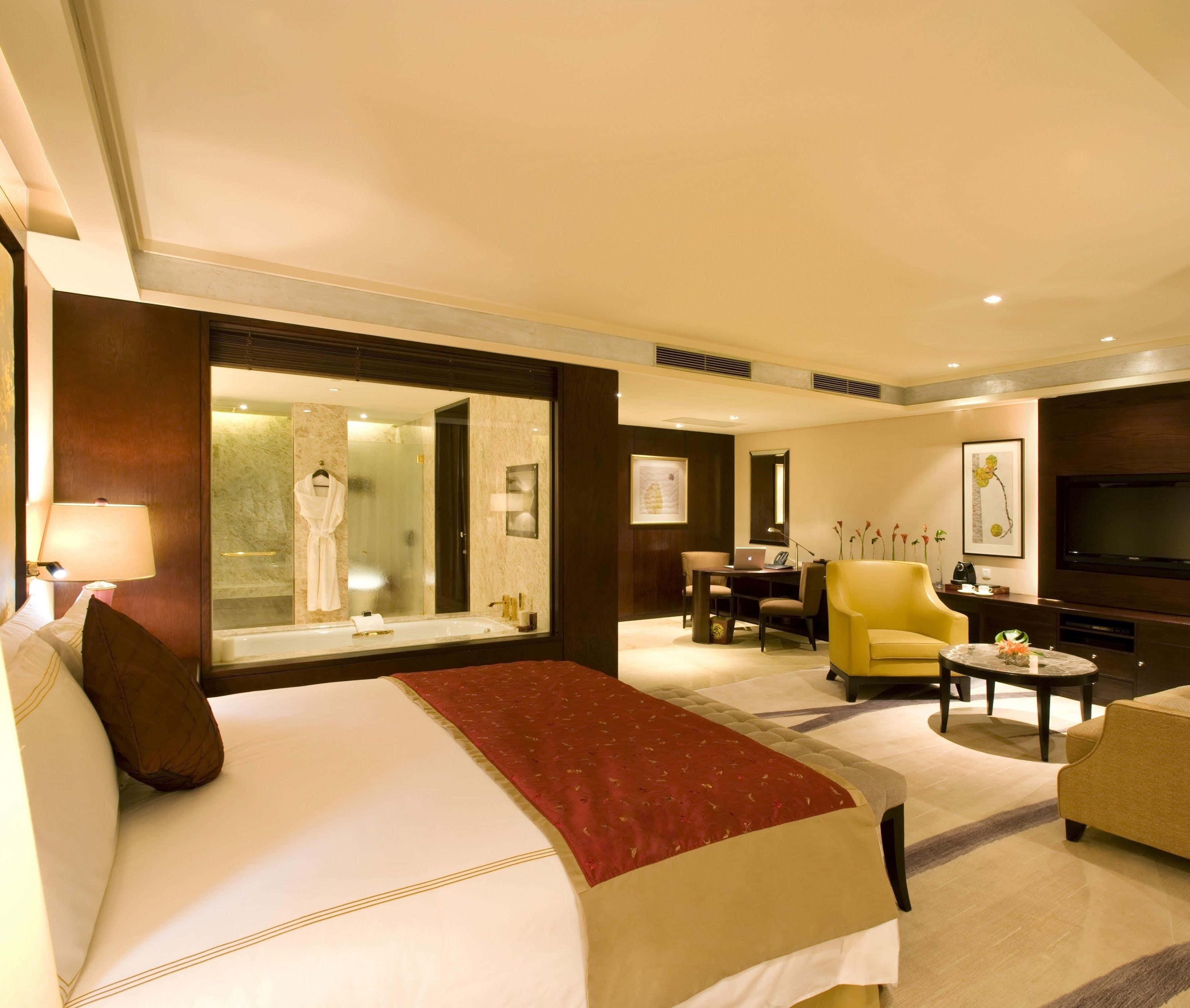 Hotel Room 桌布 壁紙 — 豪華酒店套房，配備大床、玻璃圍封浴室及現代家具，在溫暖環境燈光下。