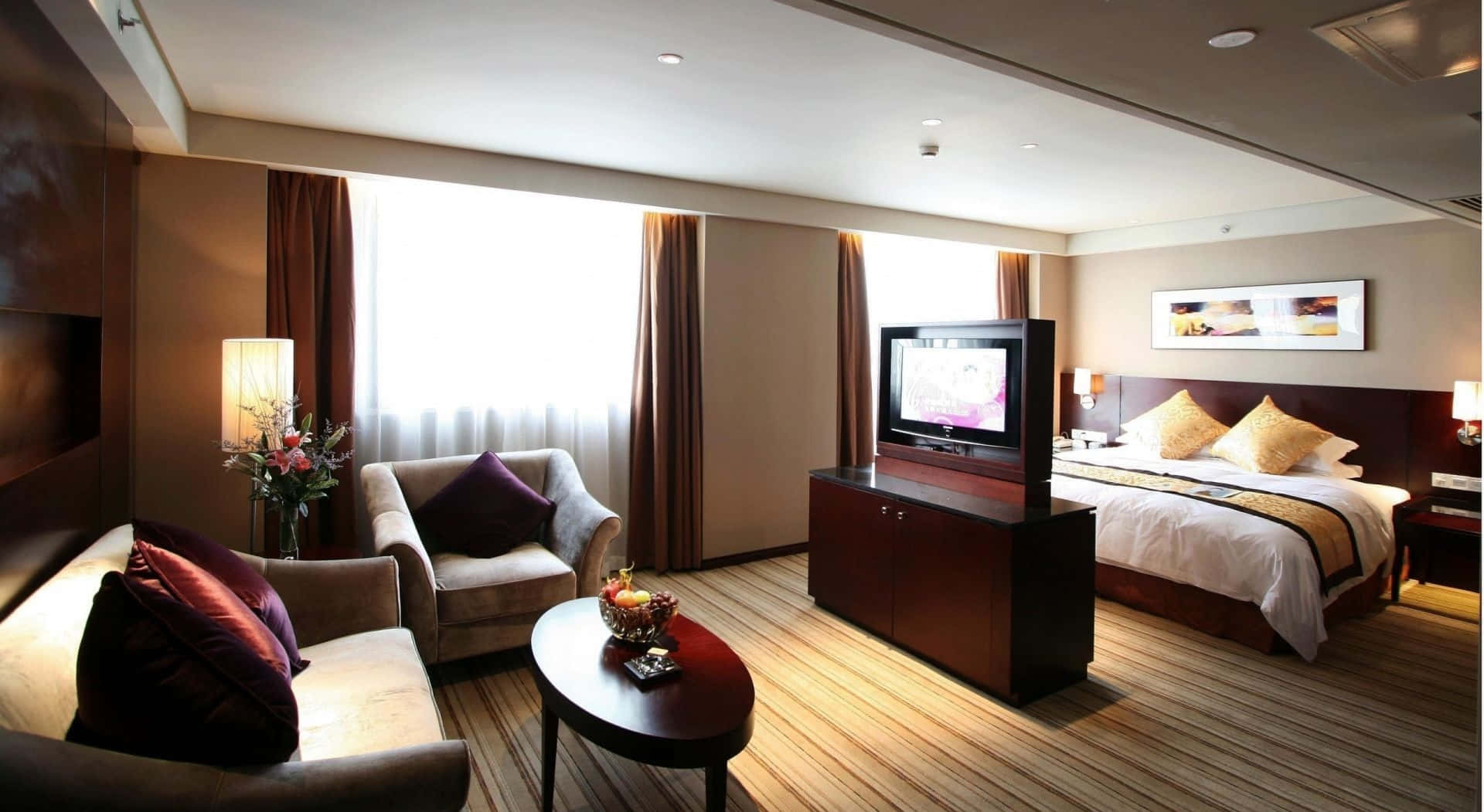 Hotel Room 桌布 壁紙 — 豪華酒店客房，舖有木地板，配備一張大床和一個舒適的休息區，沐浴在柔和自然光中。