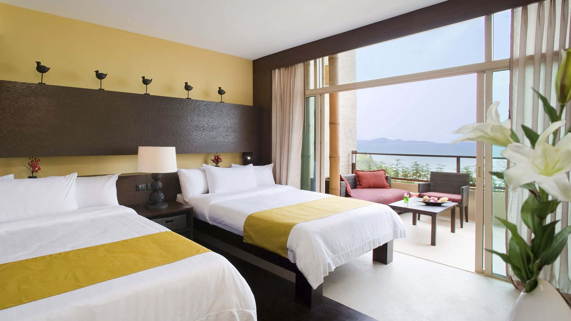 Hotel Room 桌布 壁紙 — 豪華酒店客房，設有兩張床、黃色點綴和可俯瞰海洋和山脈的陽台。