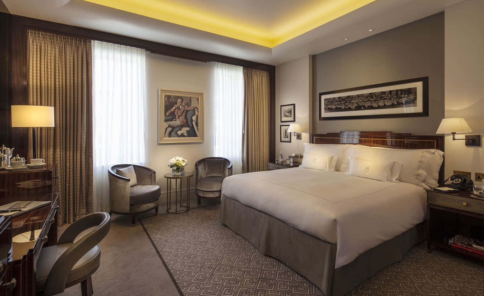Hotel Room 桌布 壁紙 — 豪華酒店客房，配備一張大床、優雅家具，以及來自天花板和床頭燈的溫暖環境照明。