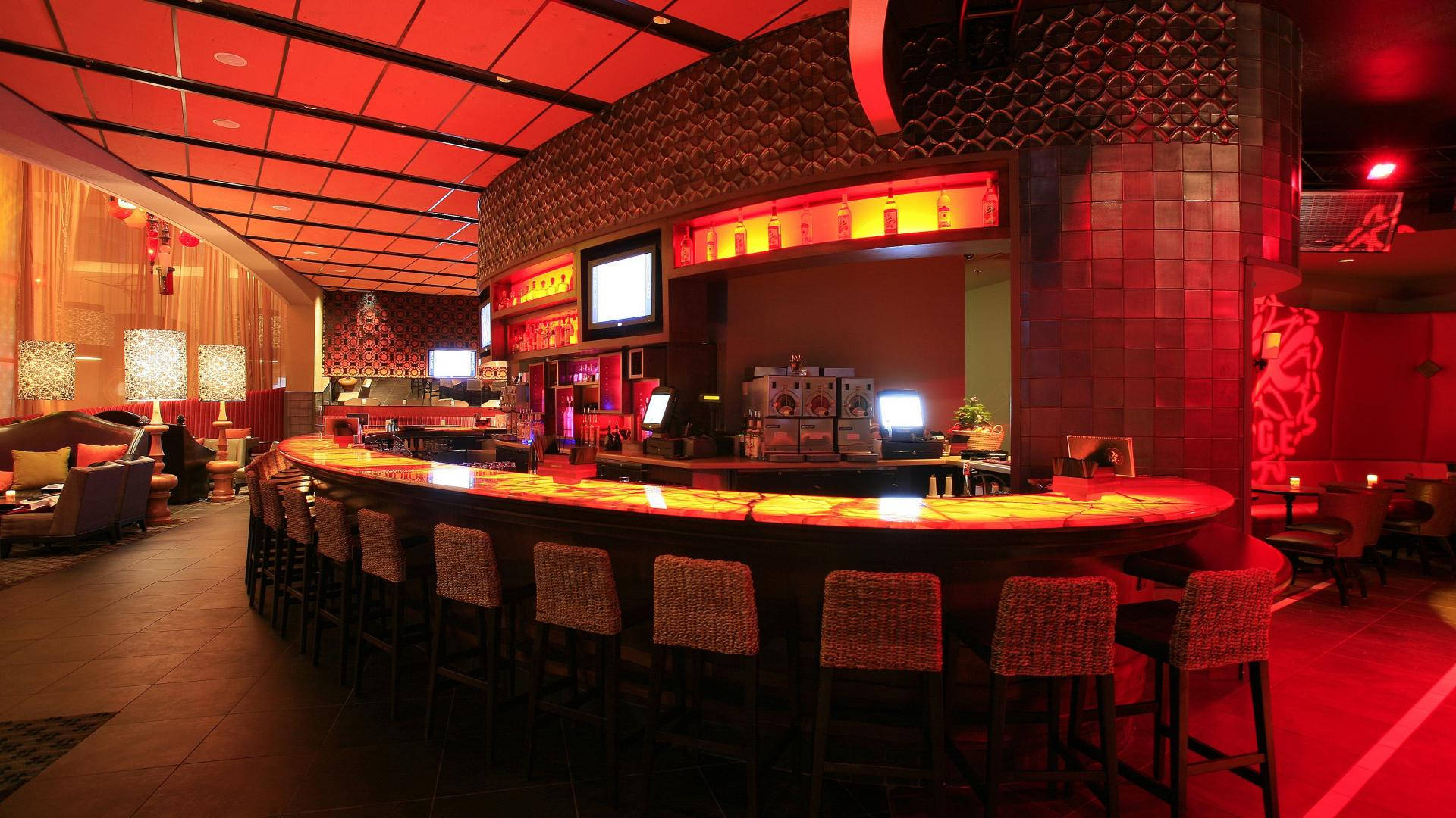 豪華酒店酒吧與餐廳 壁紙 — 一個時尚的弧形酒吧，沐浴在溫暖的紅色光芒中，配有編織凳和環境照明，營造出精緻的休息室氛圍。