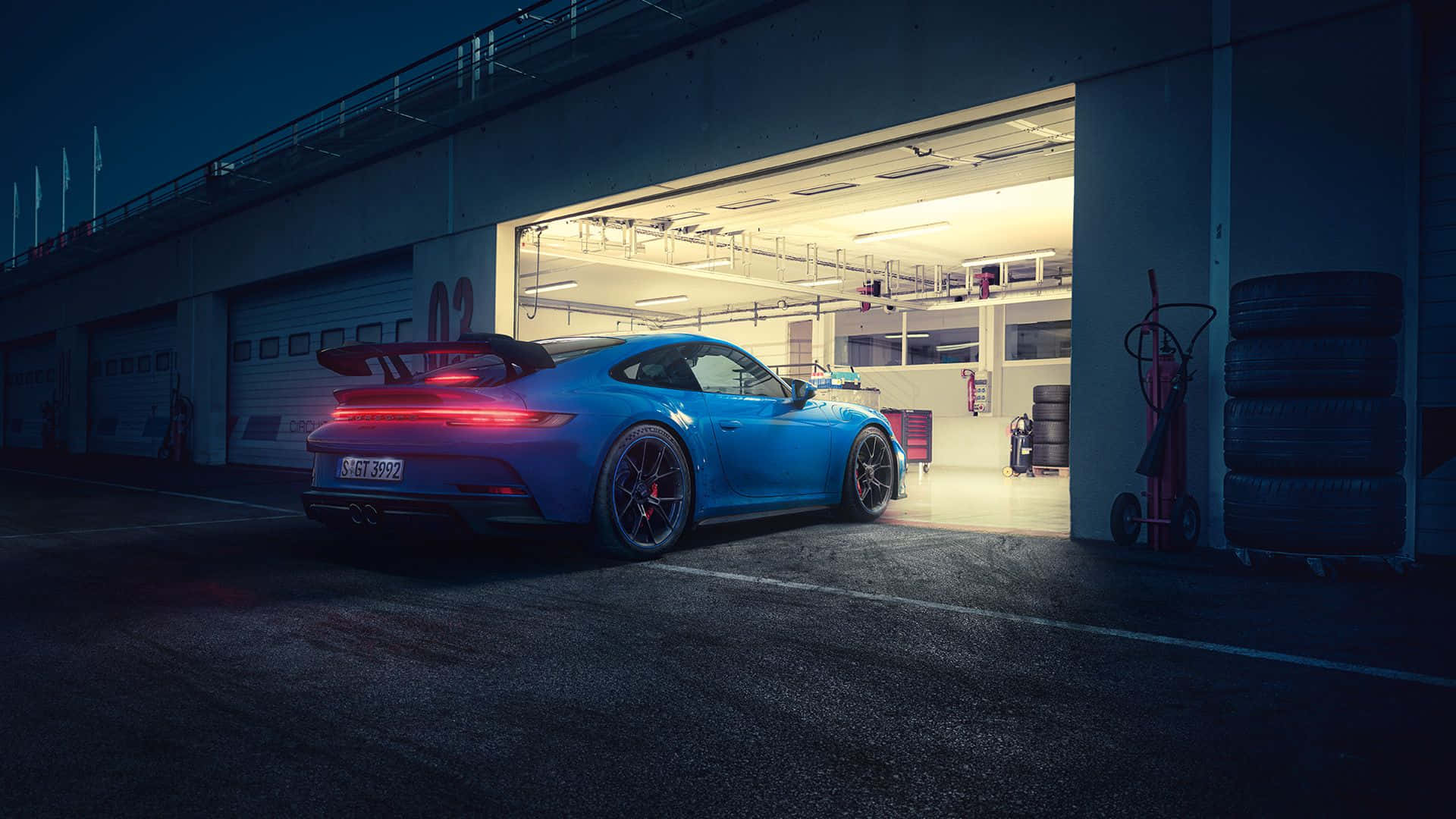 藍色保時捷 GT3 RS 夜間駛出車庫，附近有賽車輪胎。