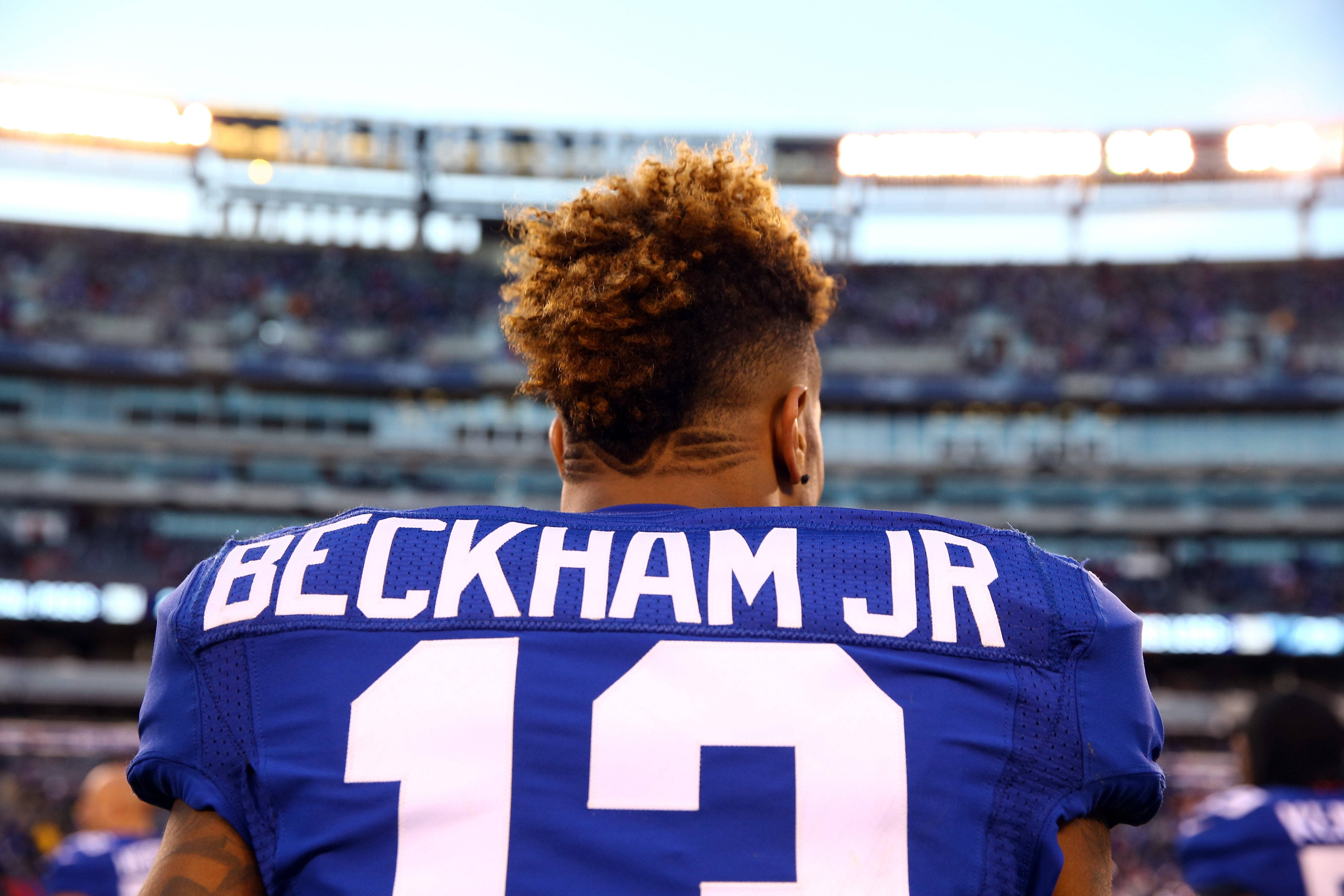 貝克漢姆小將紐約巨人的形象 壁紙 — 一名身穿藍色 Beckham Jr 13 球衣的美式足球員背對鏡頭站在夕陽下的球場。