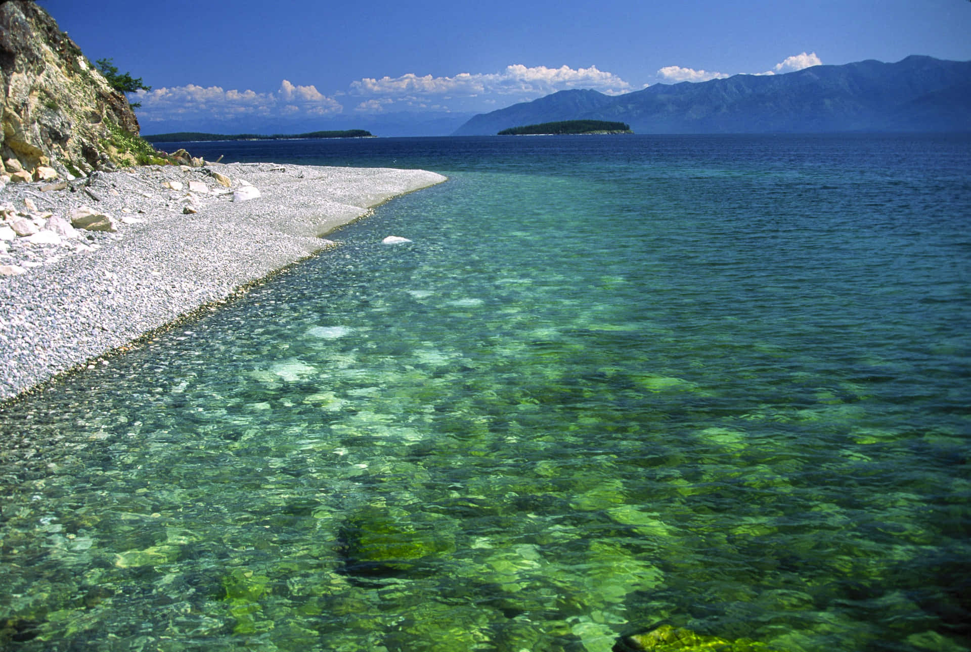 海岸線，清澈的綠色海水，遠處山巒，藍天。
