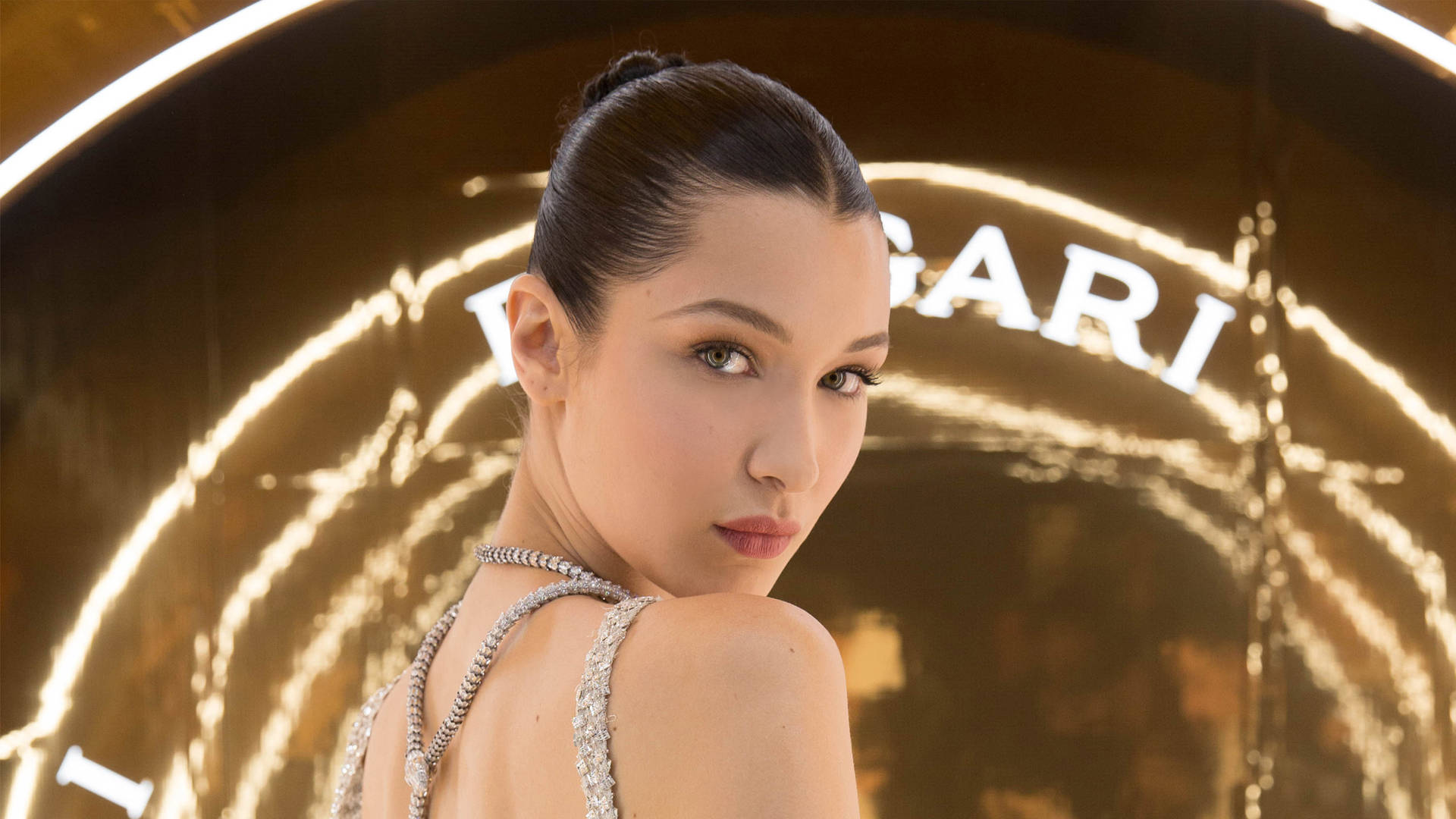 一位身穿鑲鑽連衣裙的女性在發光的Bvlgari標誌前擺姿勢。