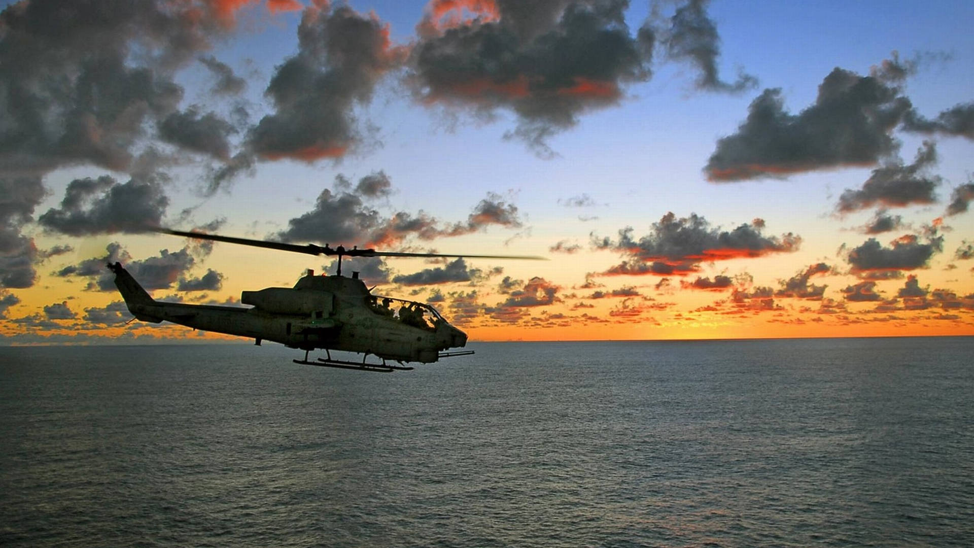 貝爾 AH-1 雷霆鷹 4K 壁紙 — 一架軍用直升機在平靜的海面上，以鮮豔的日落天空為背景呈現剪影。