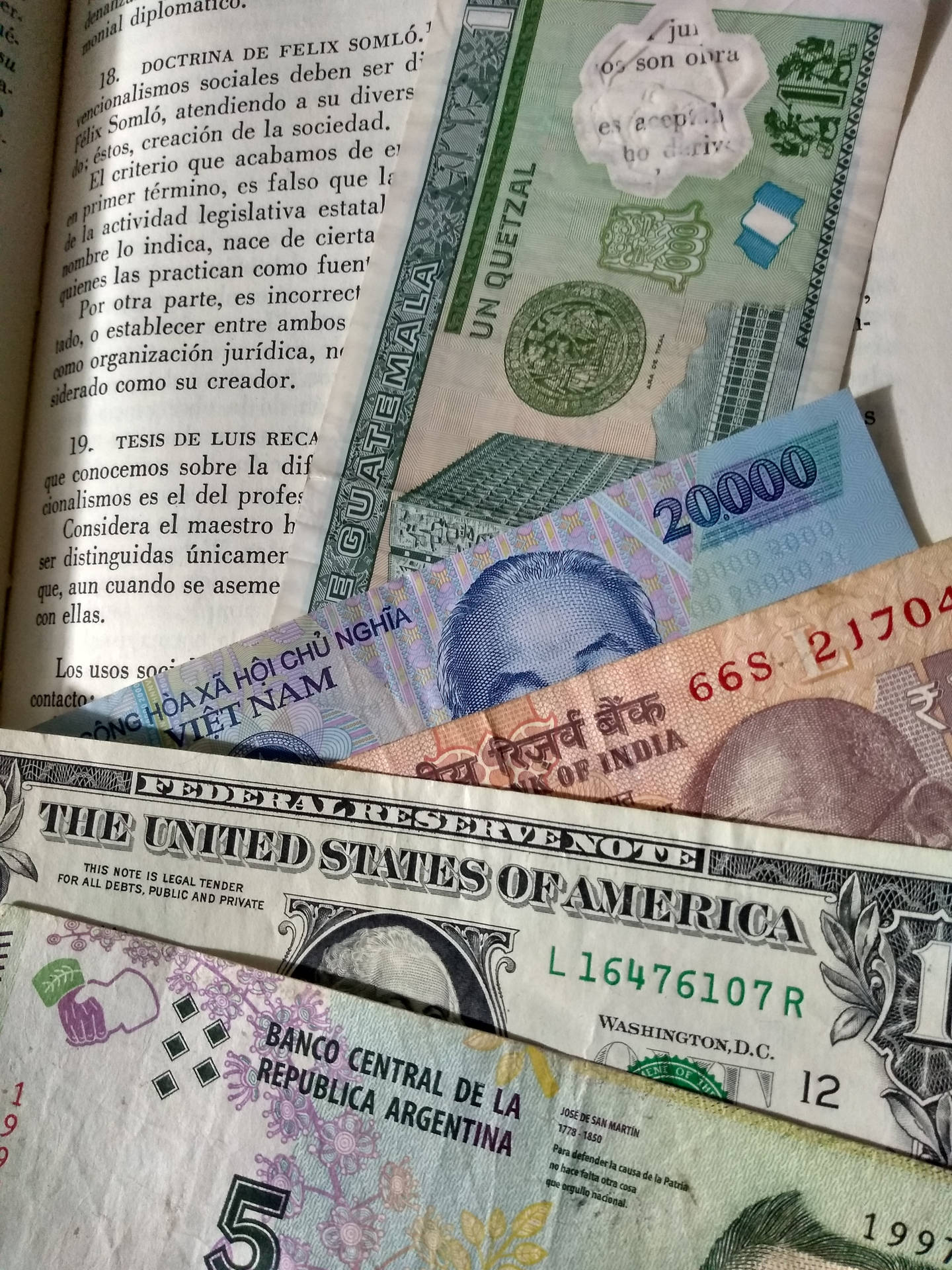 一堆國際貨幣紙幣放在一本帶有西班牙語文字的打開的書上。
