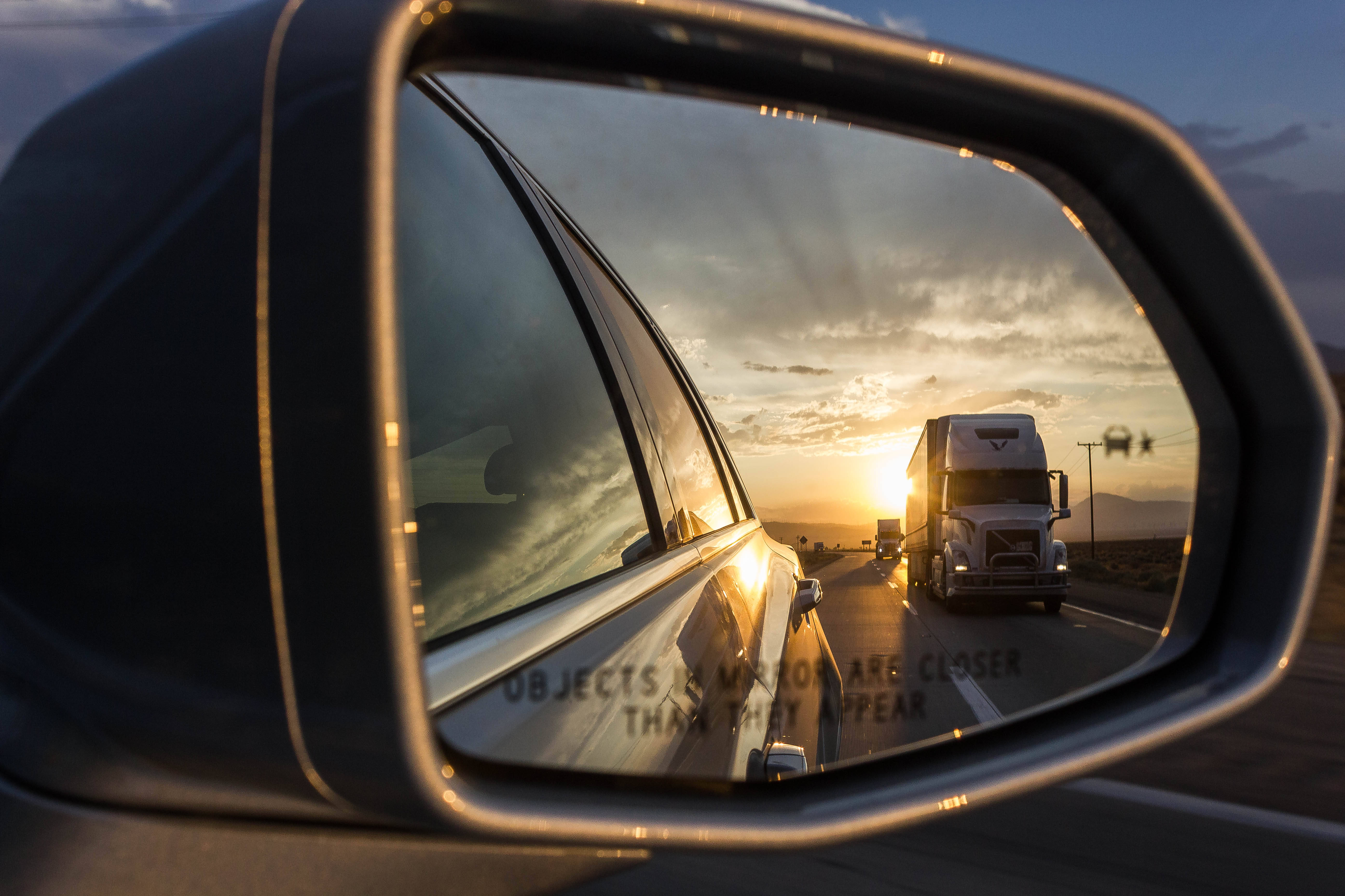 貨車在車側鏡中的倒影 壁紙 — 汽車的側鏡反射出在沙漠公路上夕陽西下時，一輛半掛卡車在溫暖的金色光芒中駛近。