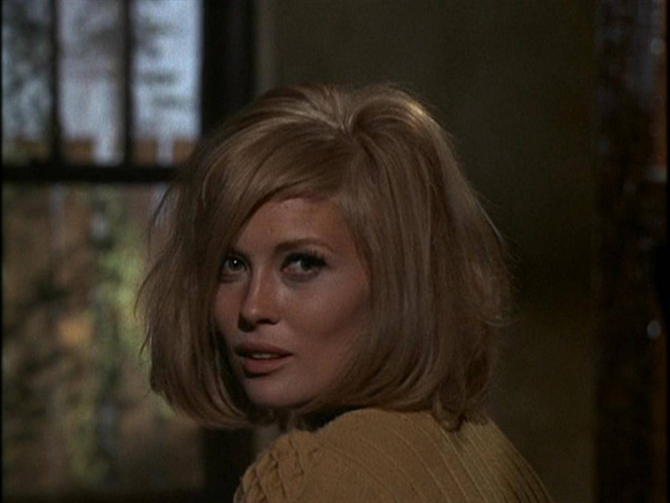 費·唐娜薇 飾 Bonnie Parker（1967 年電影） 壁紙 — 一位留著金色鮑伯頭的女士在身後有窗戶的昏暗房間裡回頭看。