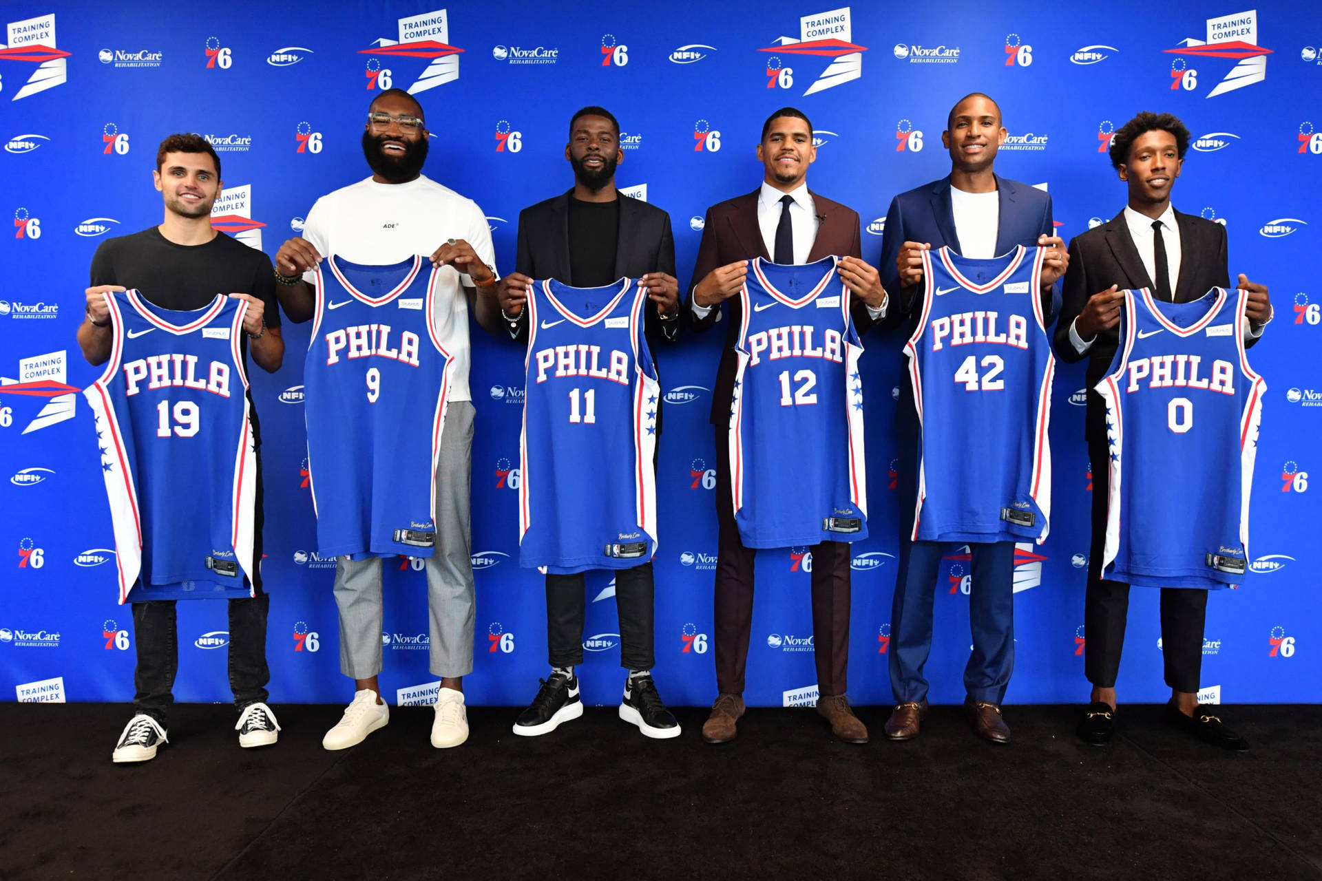 六名籃球運動員在品牌牆前舉起藍色費城76人球衣。