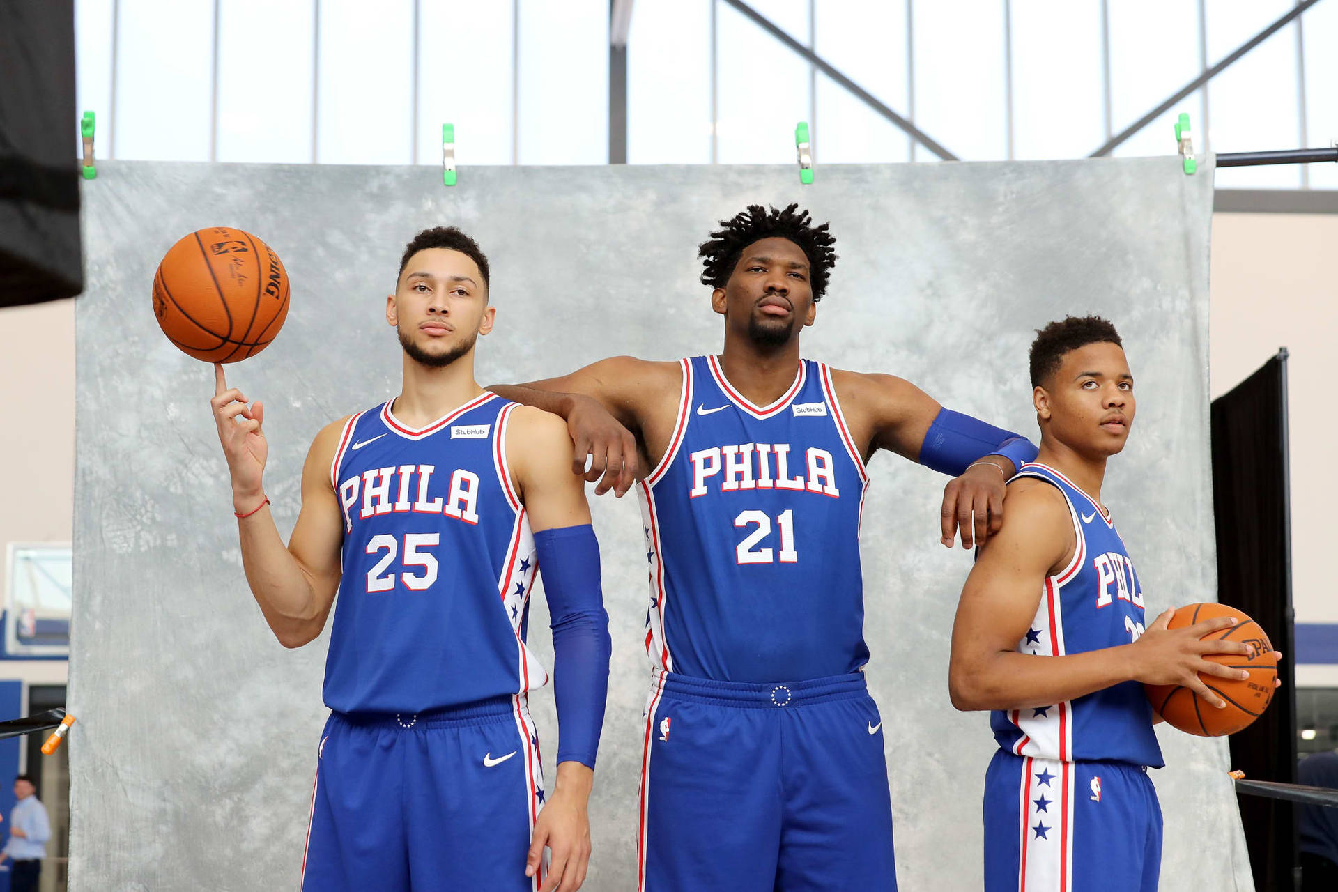 三名身穿藍色球衣的NBA籃球運動員在攝影棚中拿著籃球擺姿勢。