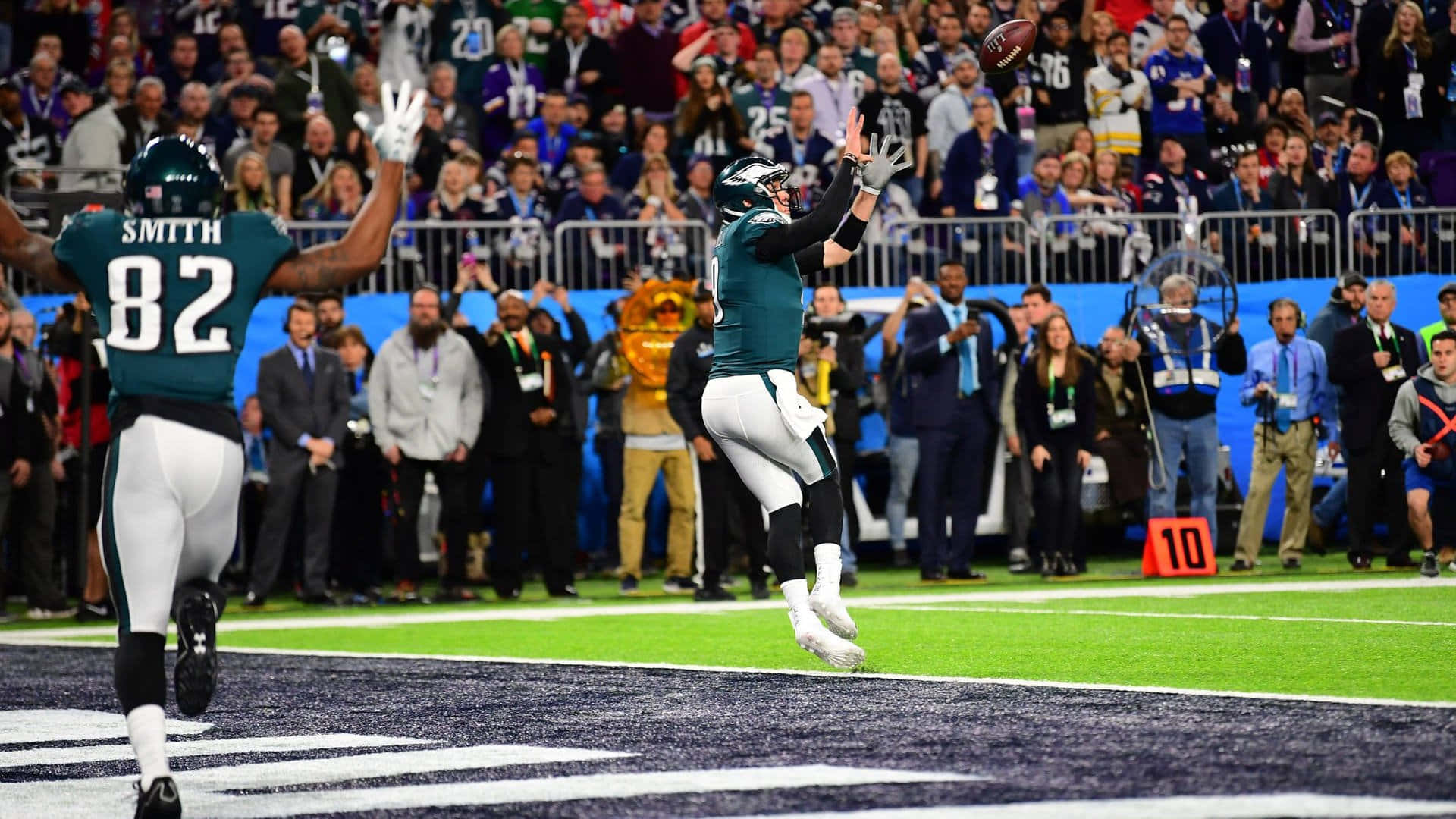 Super Bowl 桌布 壁紙 — 費城老鷹隊的外接手跳起接住橄欖球，隊友在擠滿觀眾的球場上慶祝。