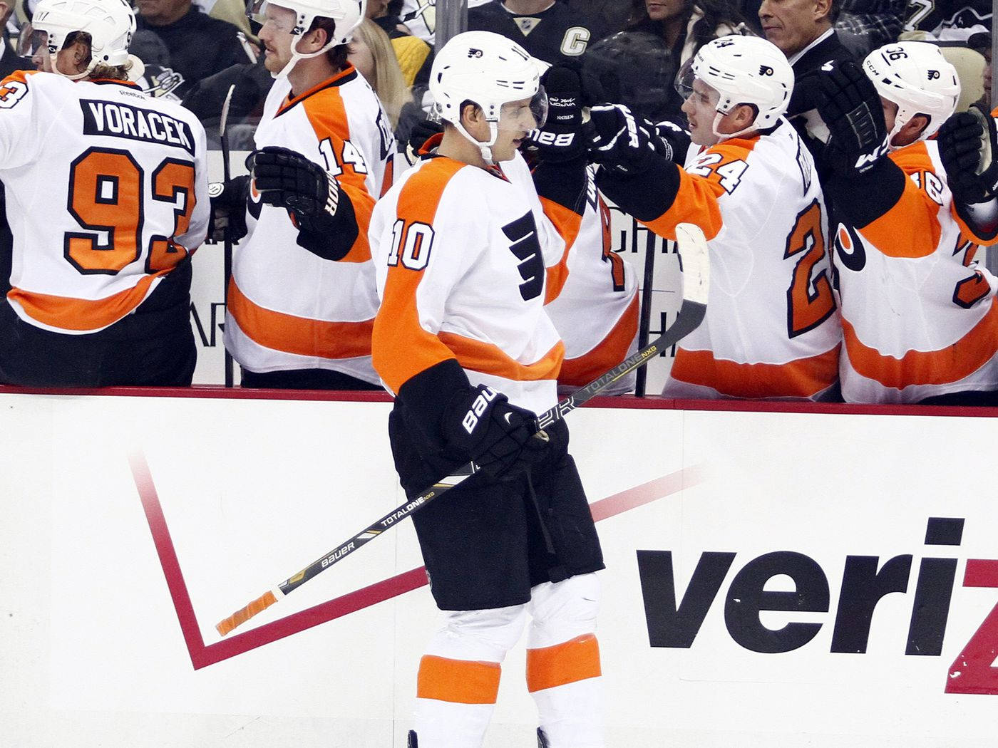 費城飛人隊布雷登·謝恩 2015 NHL 賽事精彩照片 壁紙 — 身穿白色和橙色球衣的曲棍球運動員在比賽期間於冰場圍板附近慶祝。