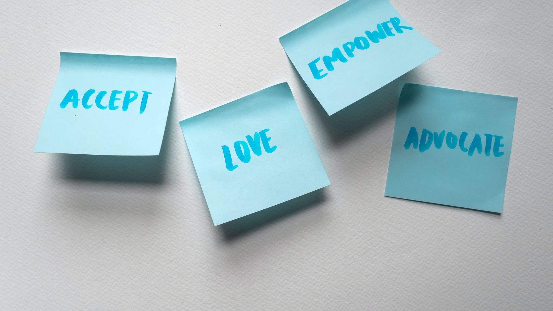 三張藍色便利貼，上面有文字 accept love empower advocate，在白色表面上。