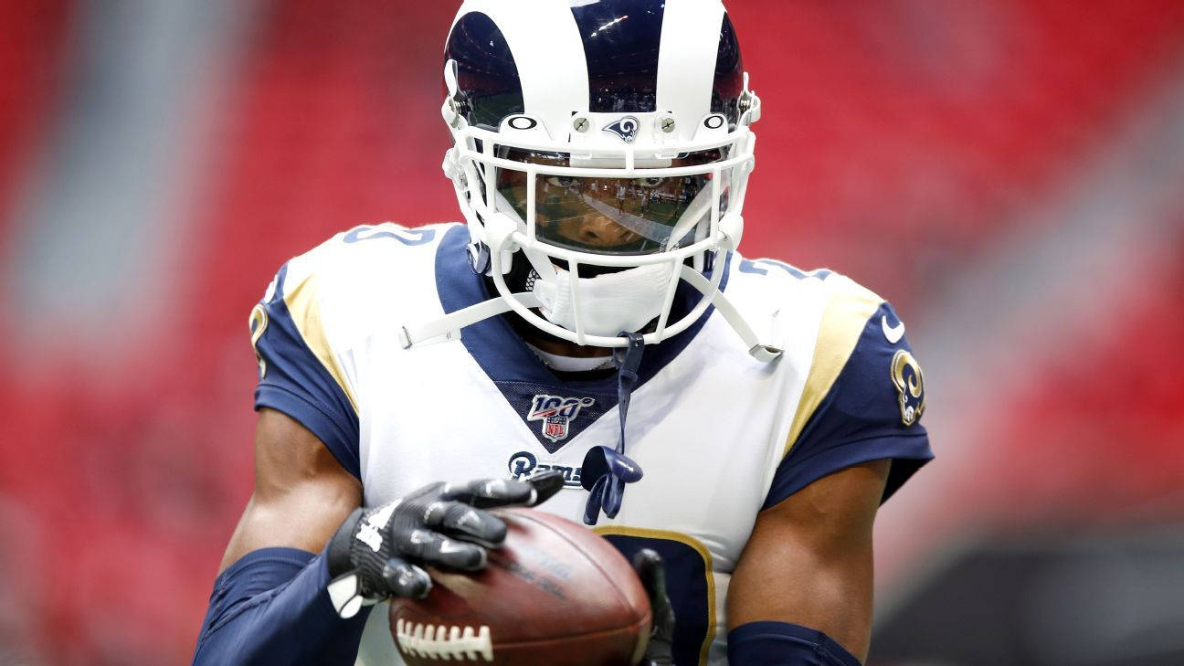 賈倫·拉姆齊堅定神情 壁紙 — 一位專注的NFL球員身穿白色和藍色的公羊隊制服，在體育場燈光下緊緊抓住橄欖球。