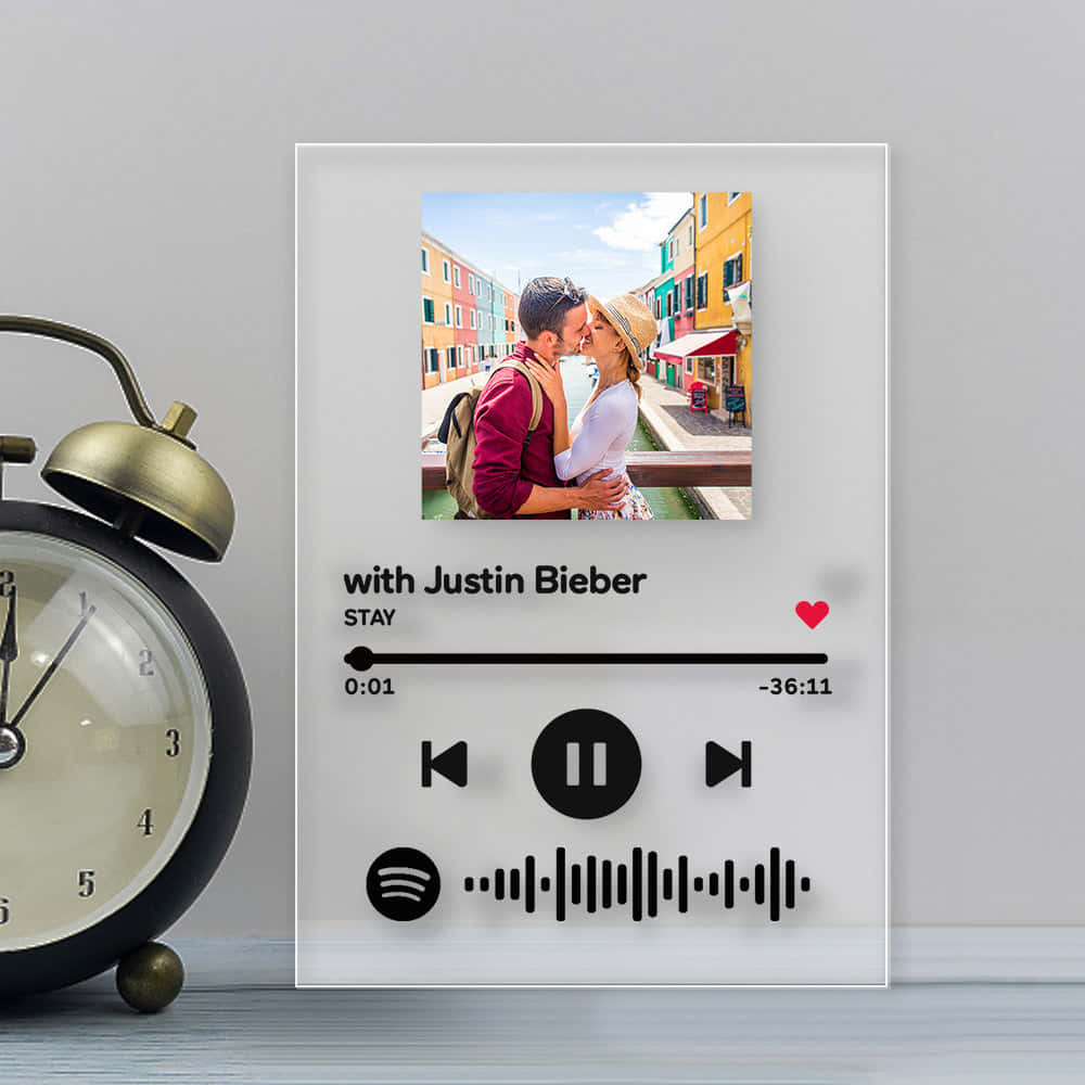 賈斯汀·比伯《Stay》歌曲截圖 壁紙 — 一個個人化的Spotify音樂播放器框架展示了一對情侶在色彩繽紛的運河邊小鎮接吻，旁邊有一個復古鬧鐘。