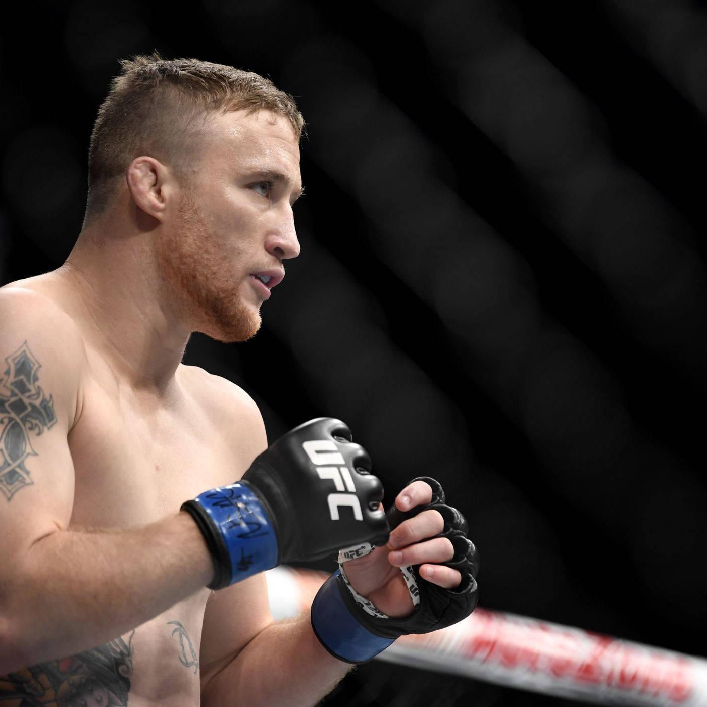 一位有紋身的男性MMA拳手戴著UFC手套站在八角籠內。