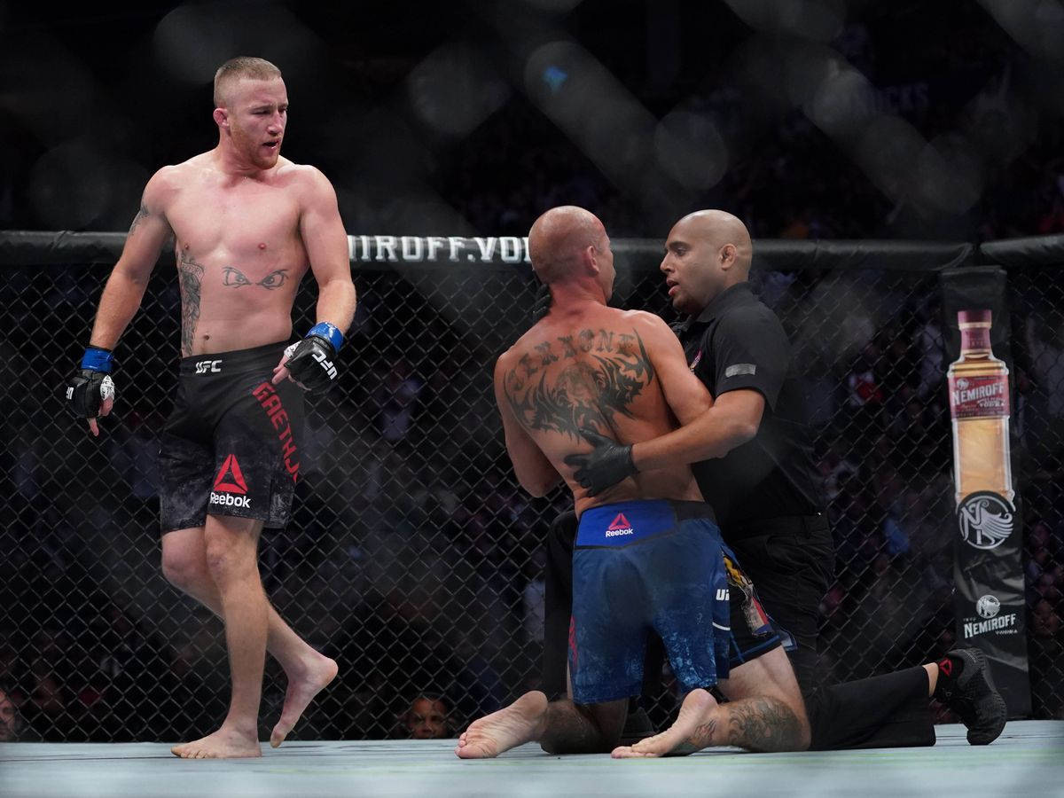 MMA拳手勝利站立，裁判停止比賽，對手在籠中跪地敗陣。