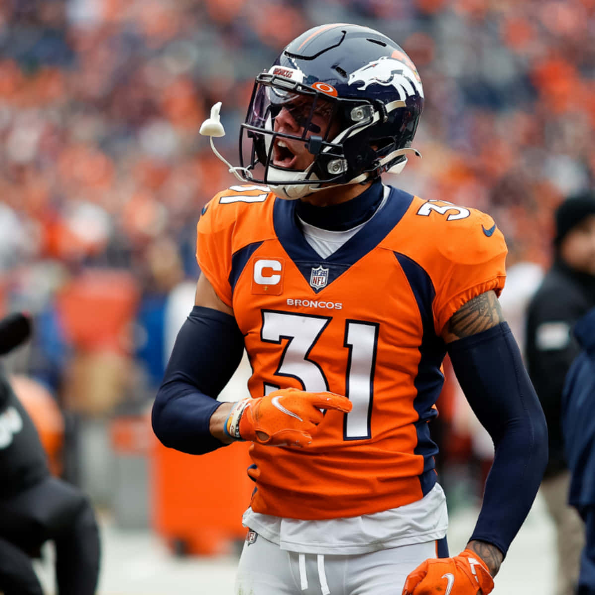 賈斯汀·西蒙斯身穿橙色球衣 壁紙 — 一名身穿橙色和海軍藍裝備的丹佛野馬隊美式足球員在比賽中激情咆哮。