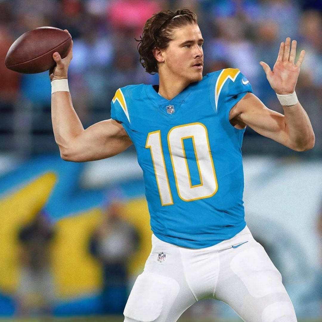 賈斯汀·赫伯特 十號球衣 壁紙 — 一位專注的NFL四分衛身穿藍色球衣，號碼10，在體育場燈光下準備在比賽中傳球。