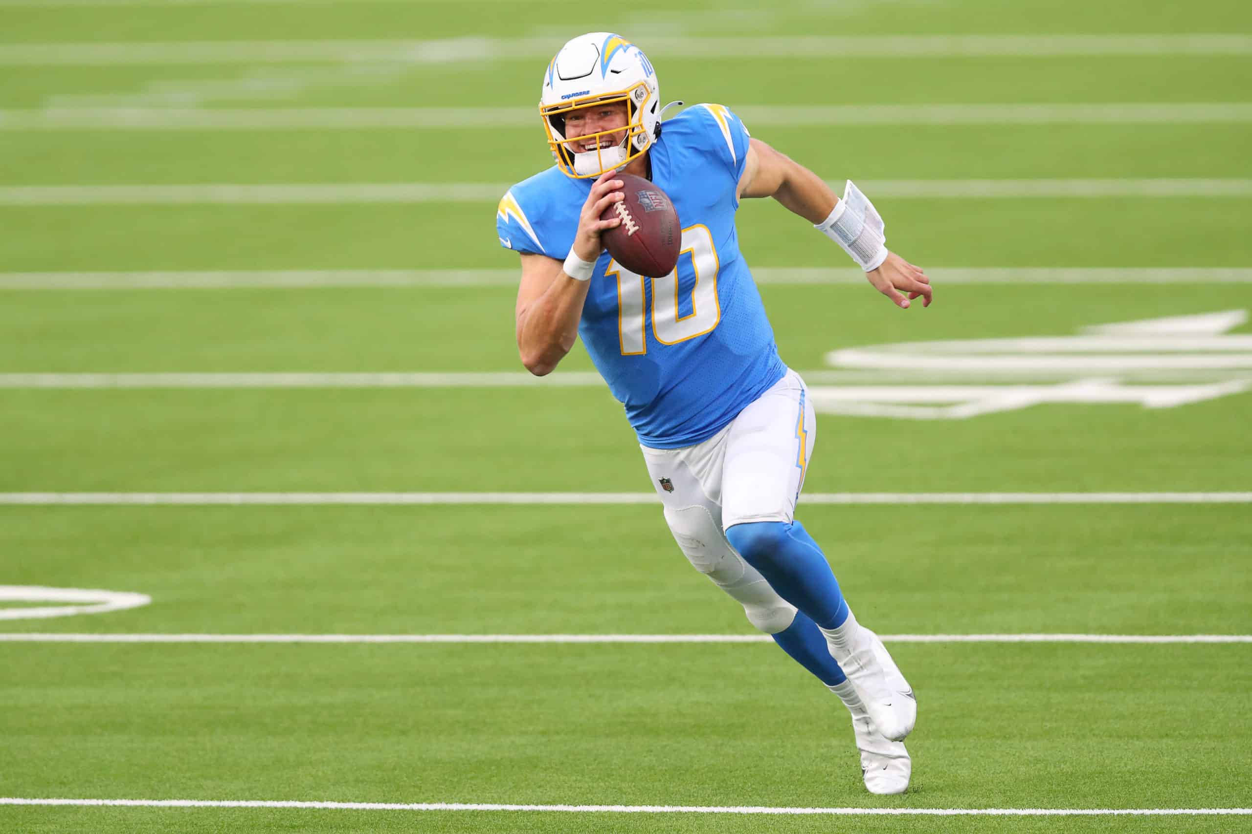 賈斯汀·赫伯特NFL 壁紙 — 一名身穿藍色球衣、號碼10的美式足球四分衛在充滿活力的綠色場地上準備投擲美式足球。