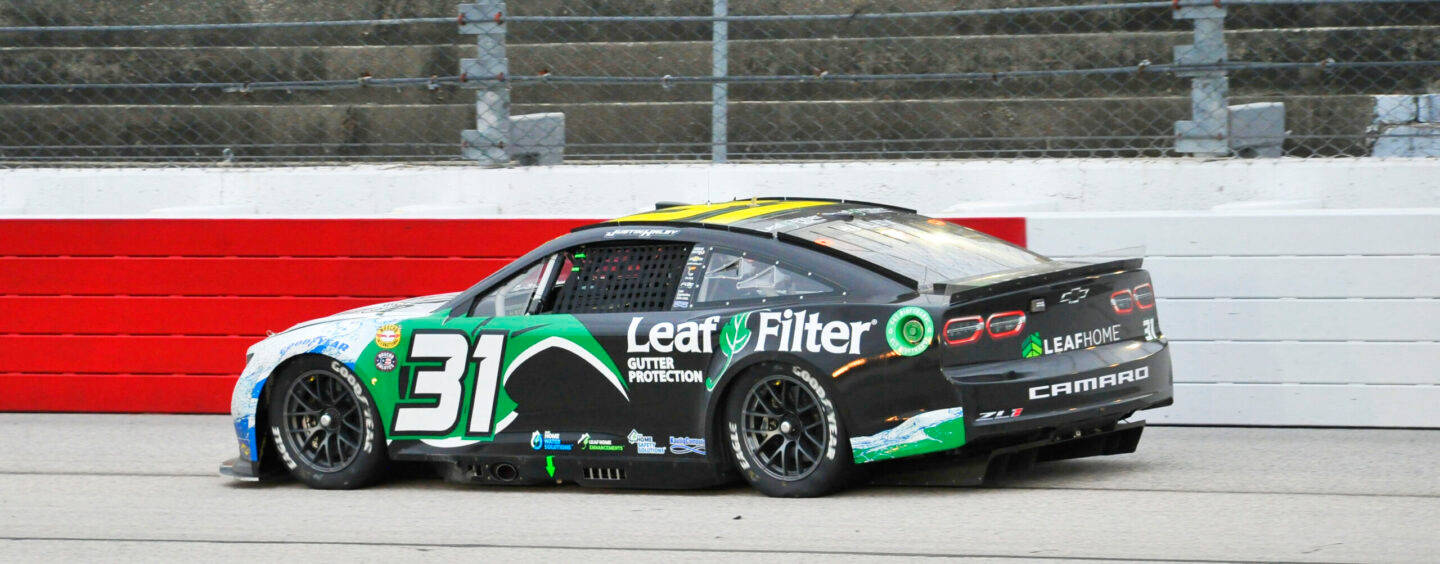 賈斯汀·黑利駕駛黑綠配色賽車 壁紙 — 一輛黑色和綠色的 #31 NASCAR 賽車，帶有 Leaf Filter 品牌標誌，在紅白相間的牆壁環繞的賽道上飛馳。