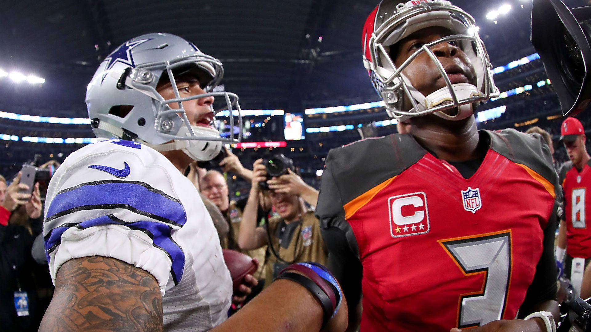 賈梅斯·溫斯頓坦帕灣海盜隊 壁紙 — 兩名戴頭盔的NFL四分衛在體育館比賽中對峙，周圍有明亮的燈光和攝影師。